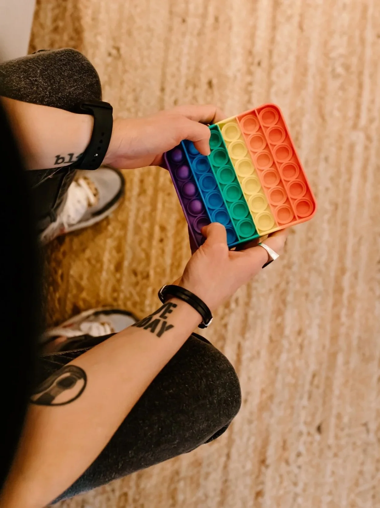 Photo from above of a person with tattooed forearms pressing buttons on a rainbow stim toy