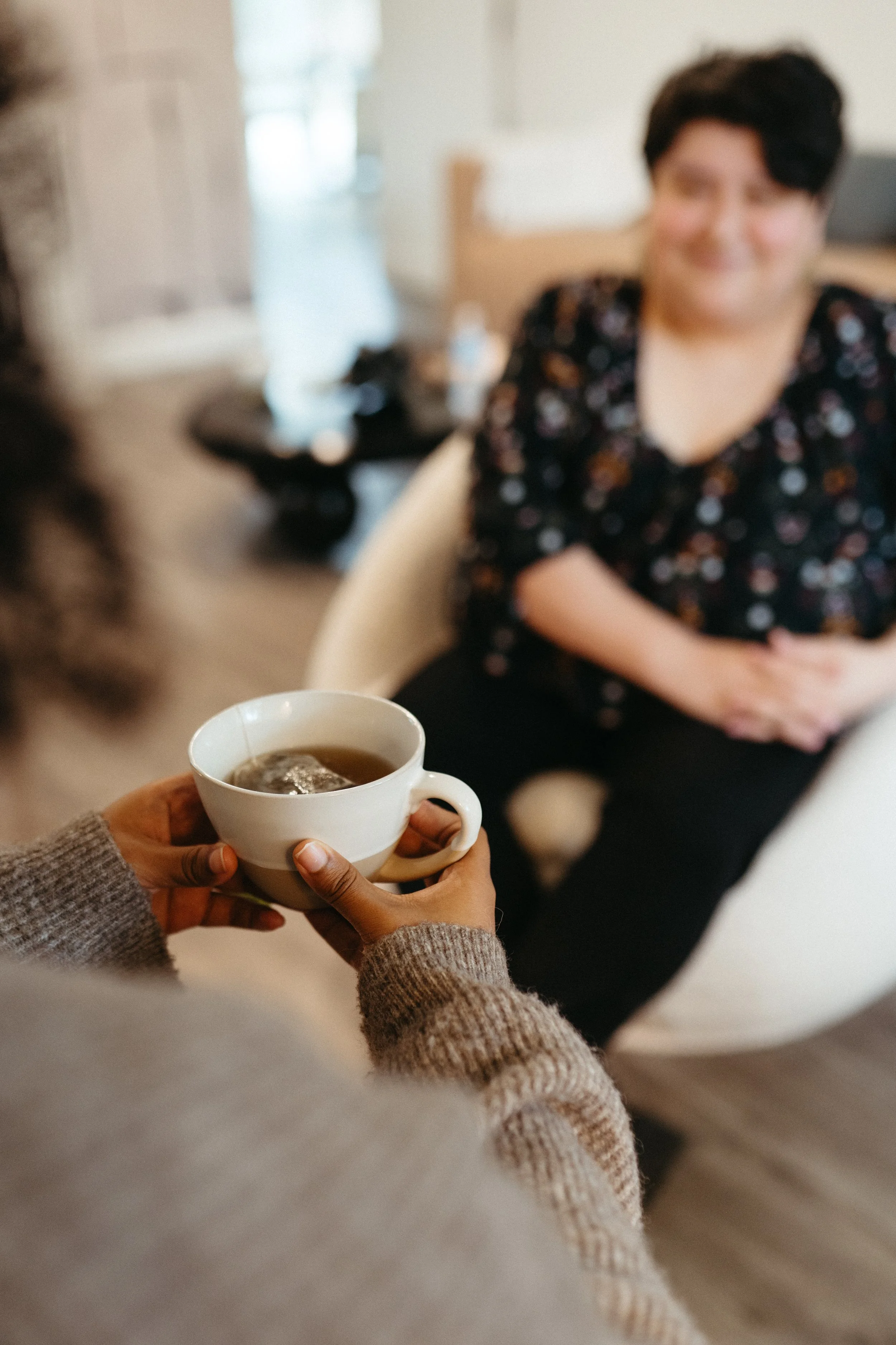 Photo of someone wearing a cozy knit sweater holding a cup of tea across from a Nido IFT therapist who smiling is out of focus