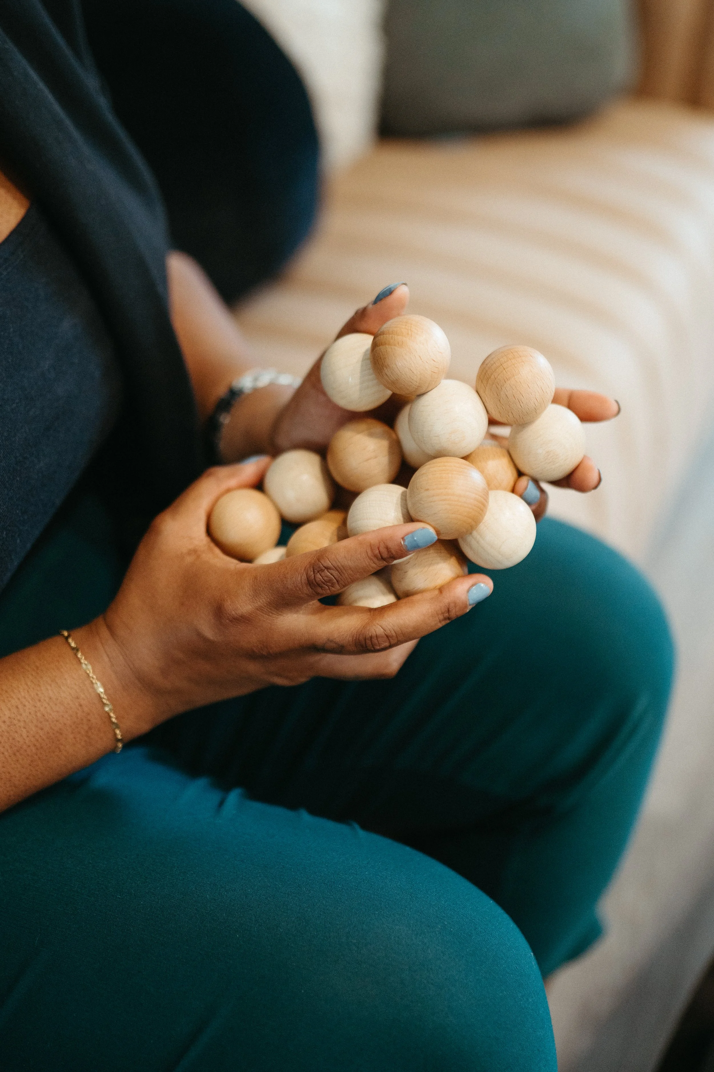 Photo of hands with blue nails and a thin gold bracelet holding several small wooden balls