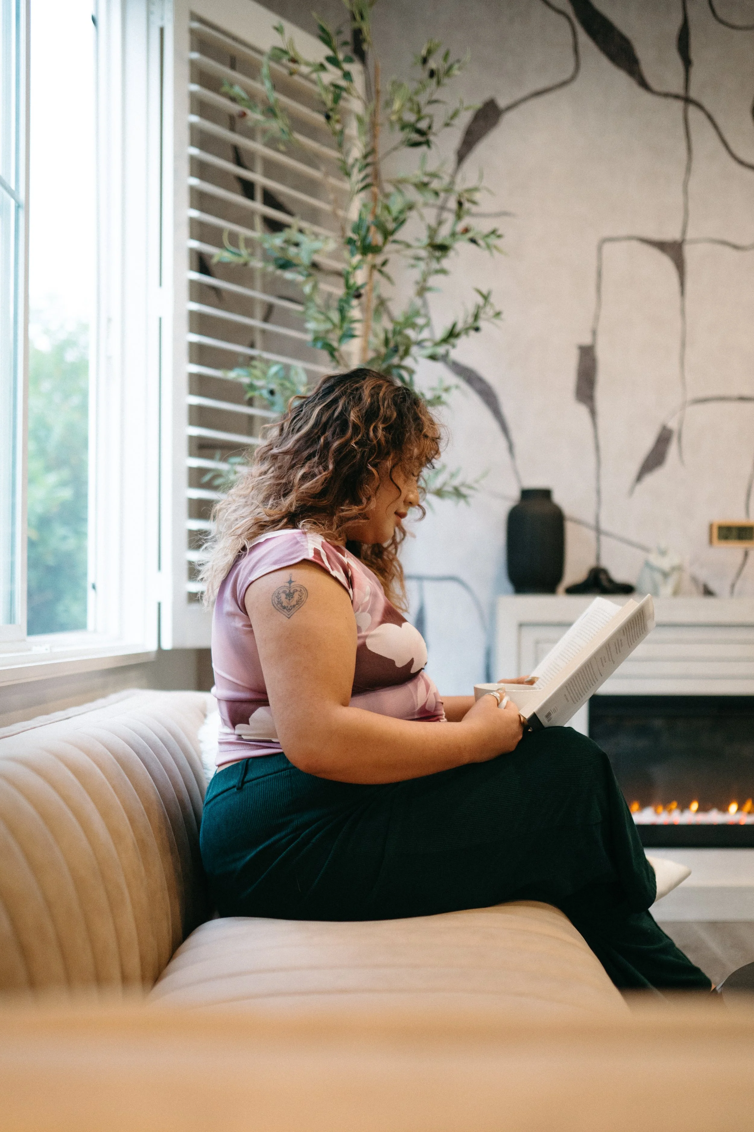 Photo of a Nido IFT therapist sitting on a couch next to a fireplace reading a book and holding a cup of tea