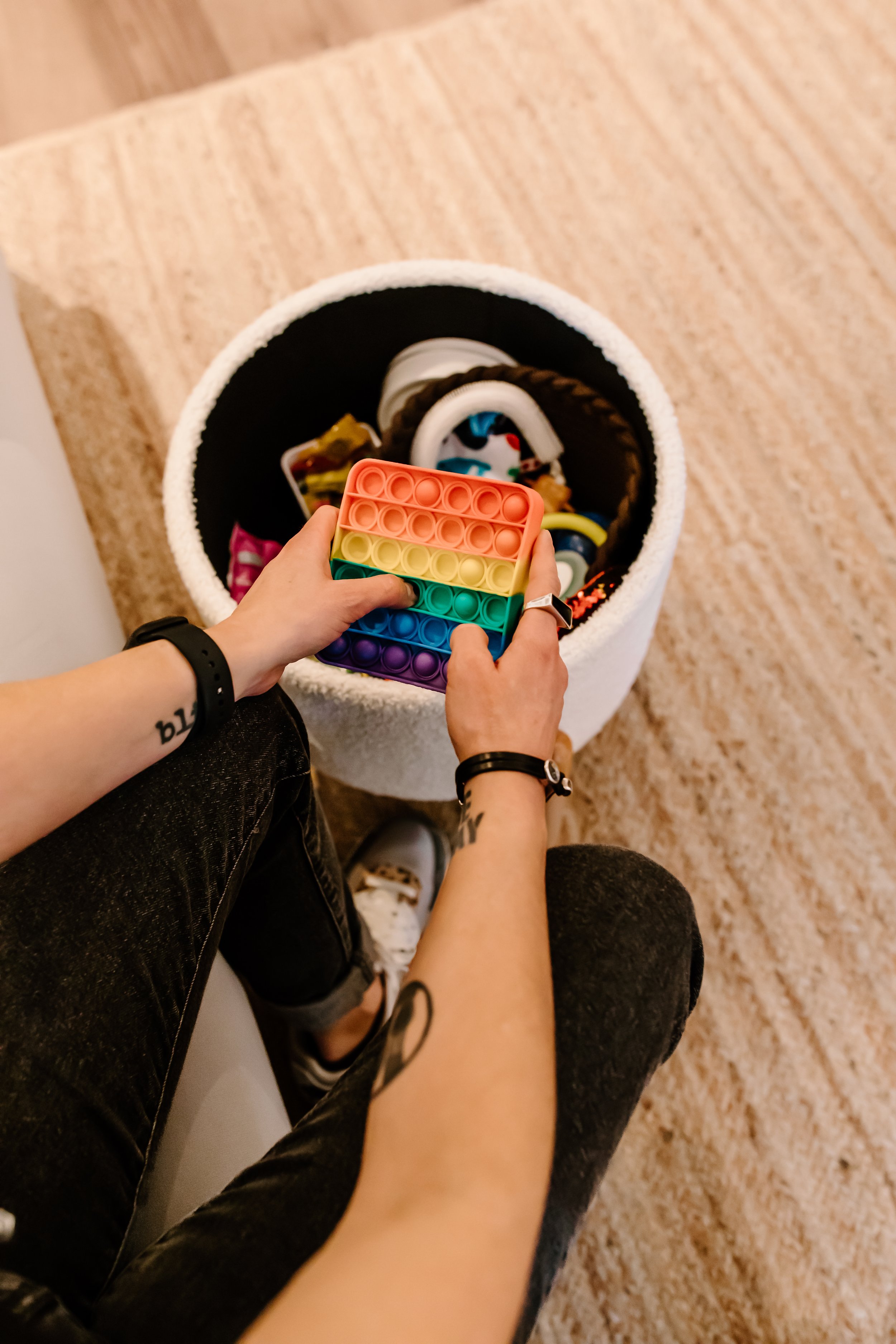Photo from above of hands playing with a rainbow colored stim toy, with a basket of other objects underneath