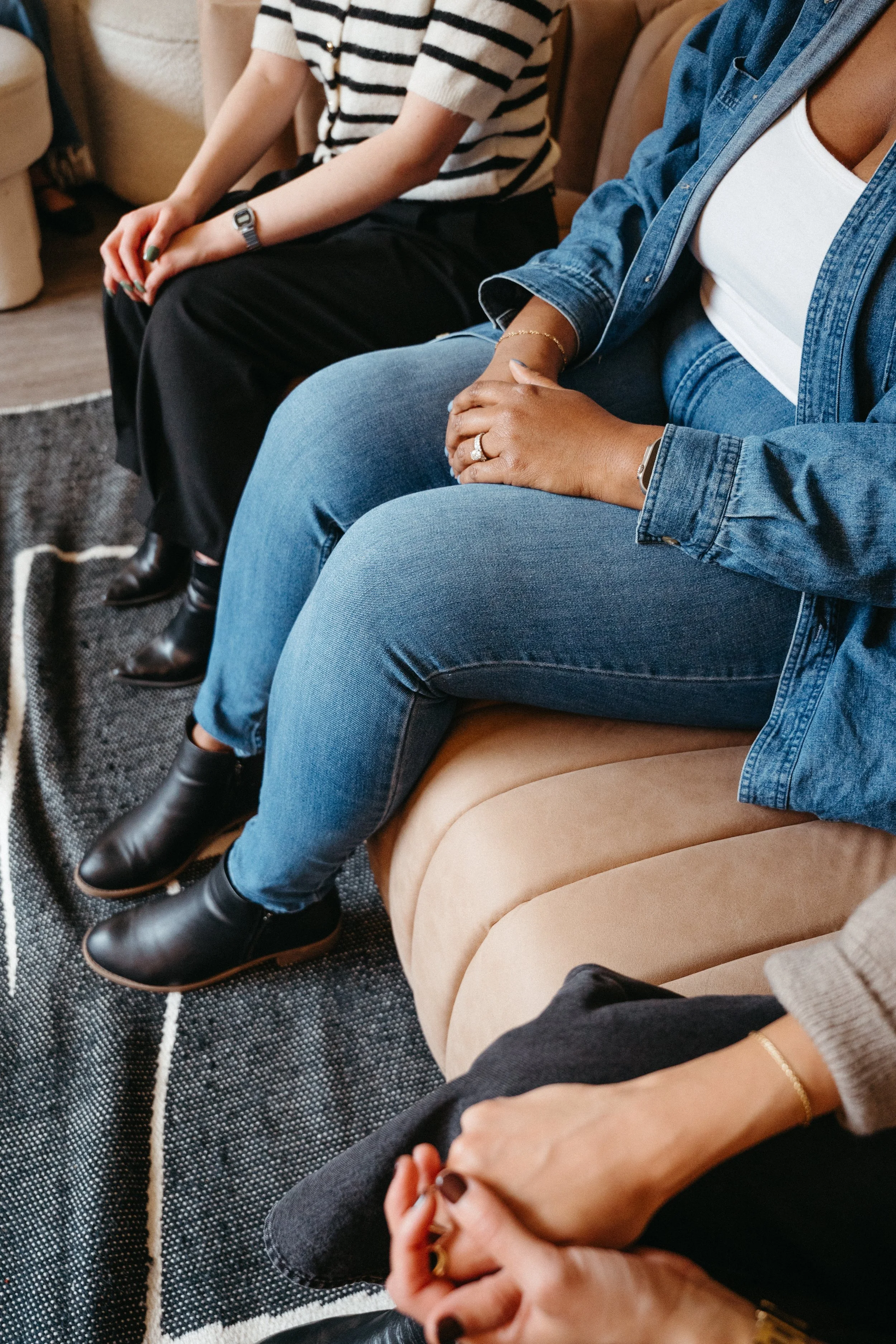 Photo of two bodies from the chest down sitting side by side on a couch next to one another with hands in their laps