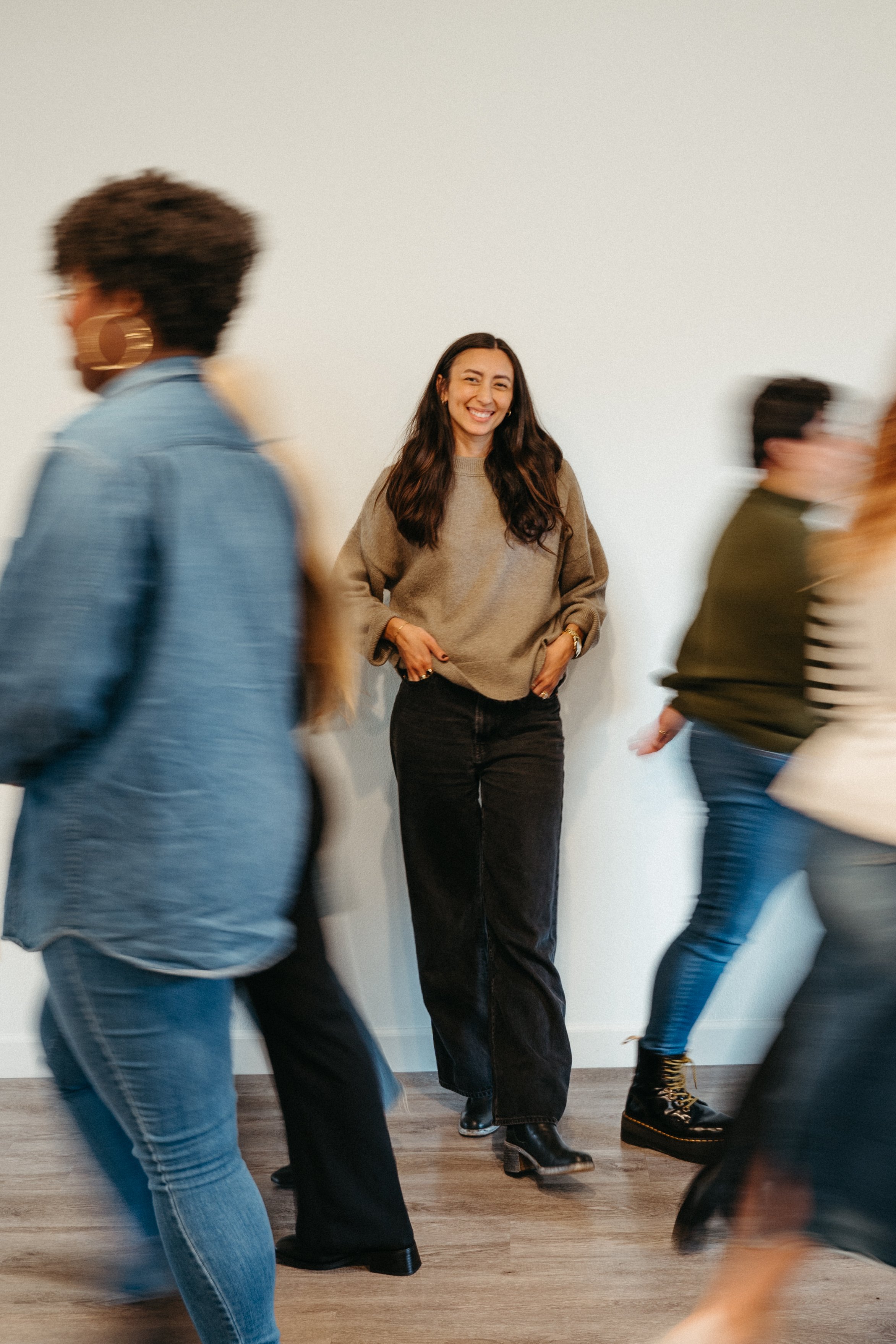 Photo focused on Nido IFT founder Sarah Finch smiling, with blurred bodies in motion walking in front of her to either side