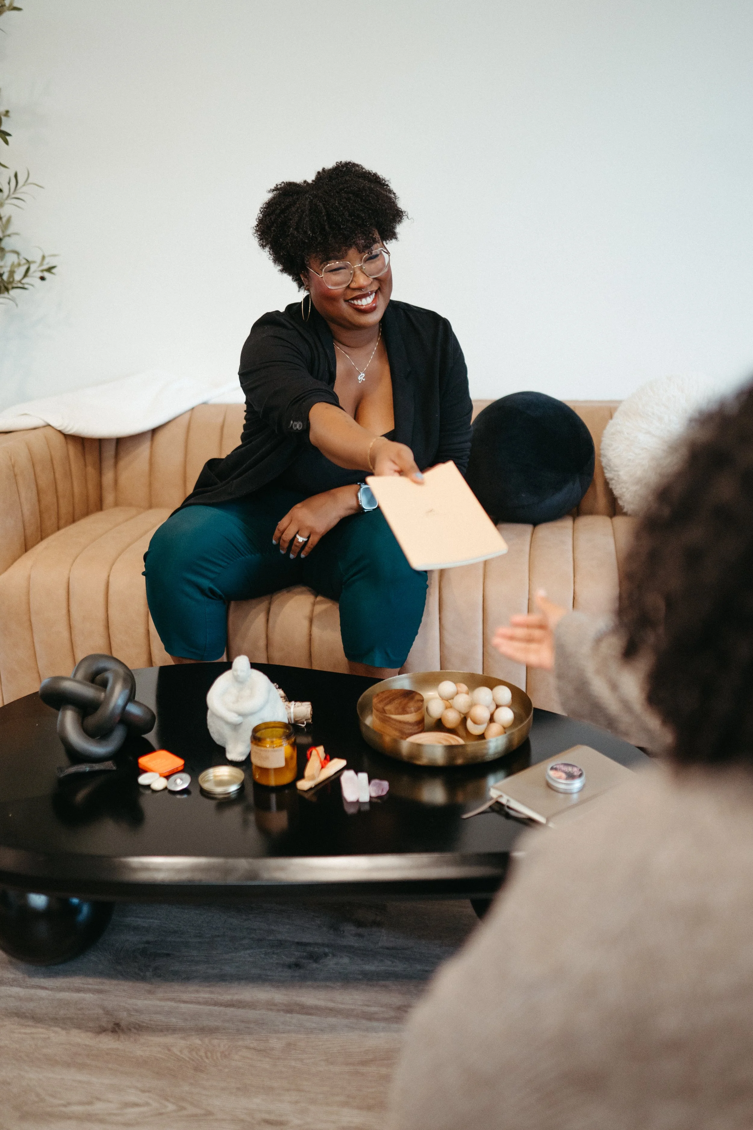 Photo of a Nido IFT therapist smiling on a couch and holding out a small journal to a client across a coffee table