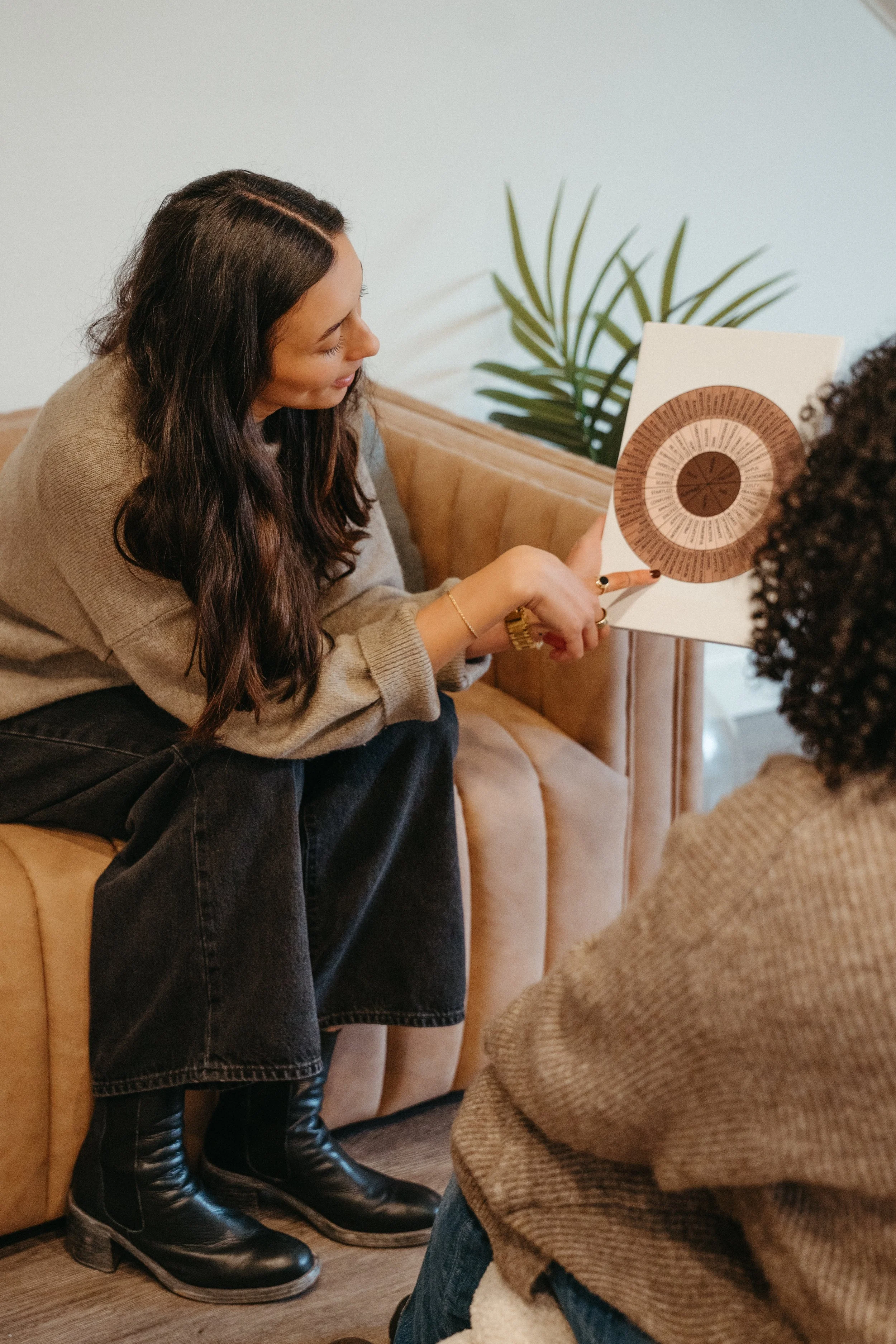 Photo of Nido IFT founder Sarah Finch sitting on a couch speaking and pointing to part of a emotion wheel chart with a pen
