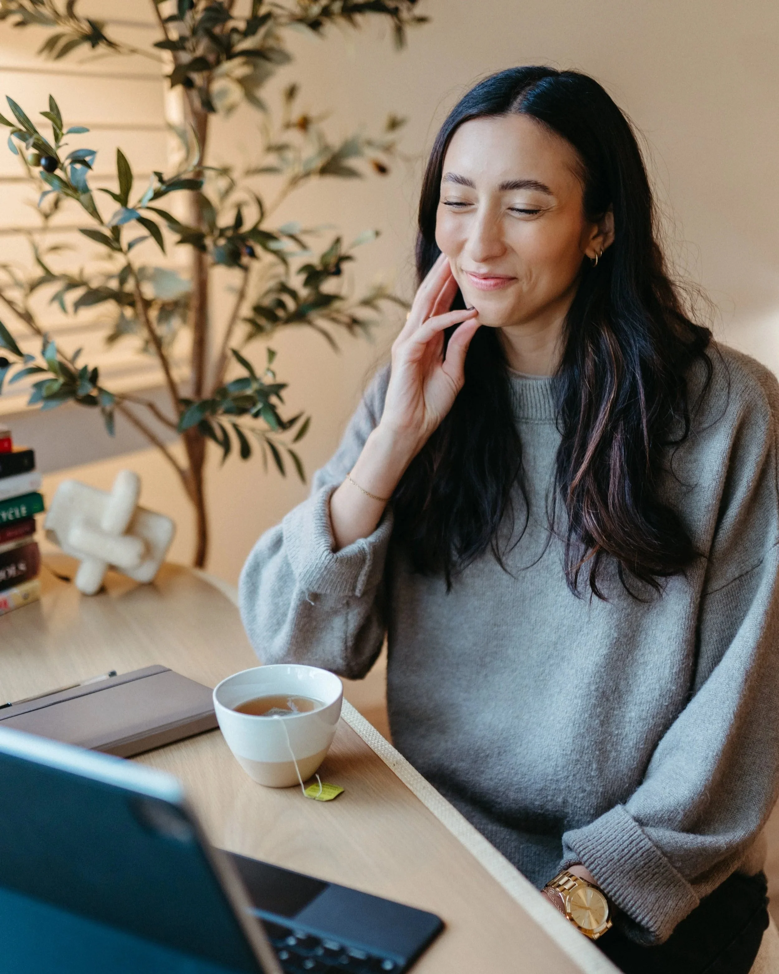 Photo of Nido IFT founder Sarah Finch smiling sitting at a desk with notebook and tea on a telehealth session