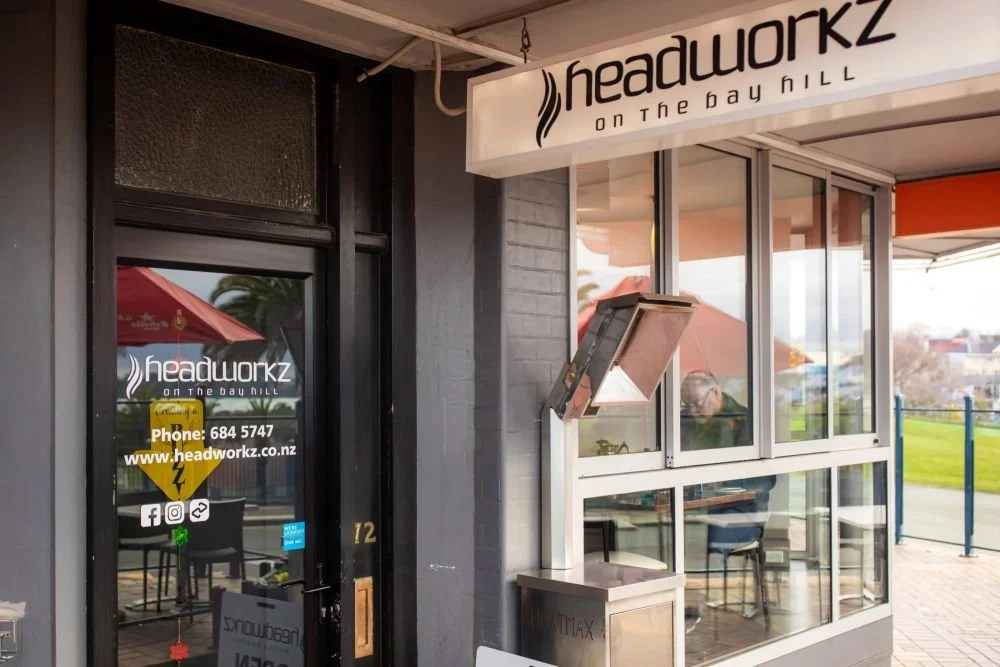 Exterior view of Headworkz, a restaurant or cafe, on the Bay Hill with glass windows and a sign displaying the business name and contact information.