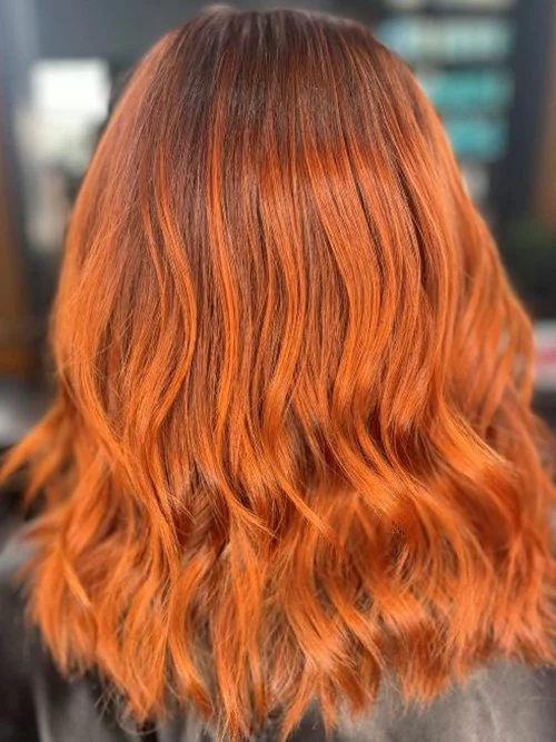 Back view of a person with shoulder-length wavy red hair.