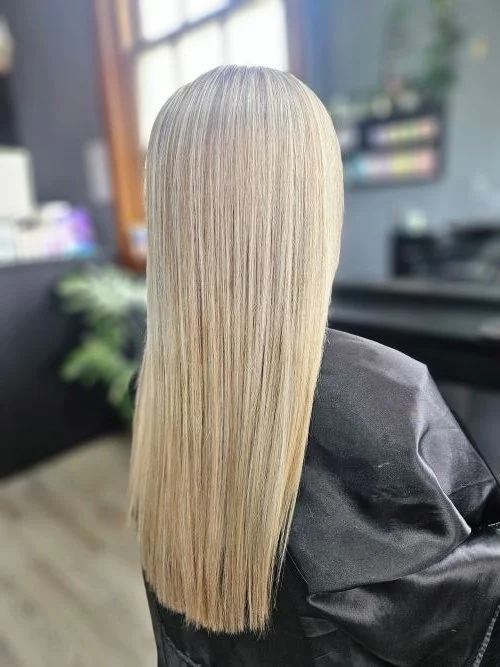 Blonde woman with straight, shiny hair sitting in a salon chair