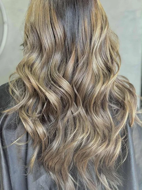 Back view of a woman with long, wavy blonde hair.