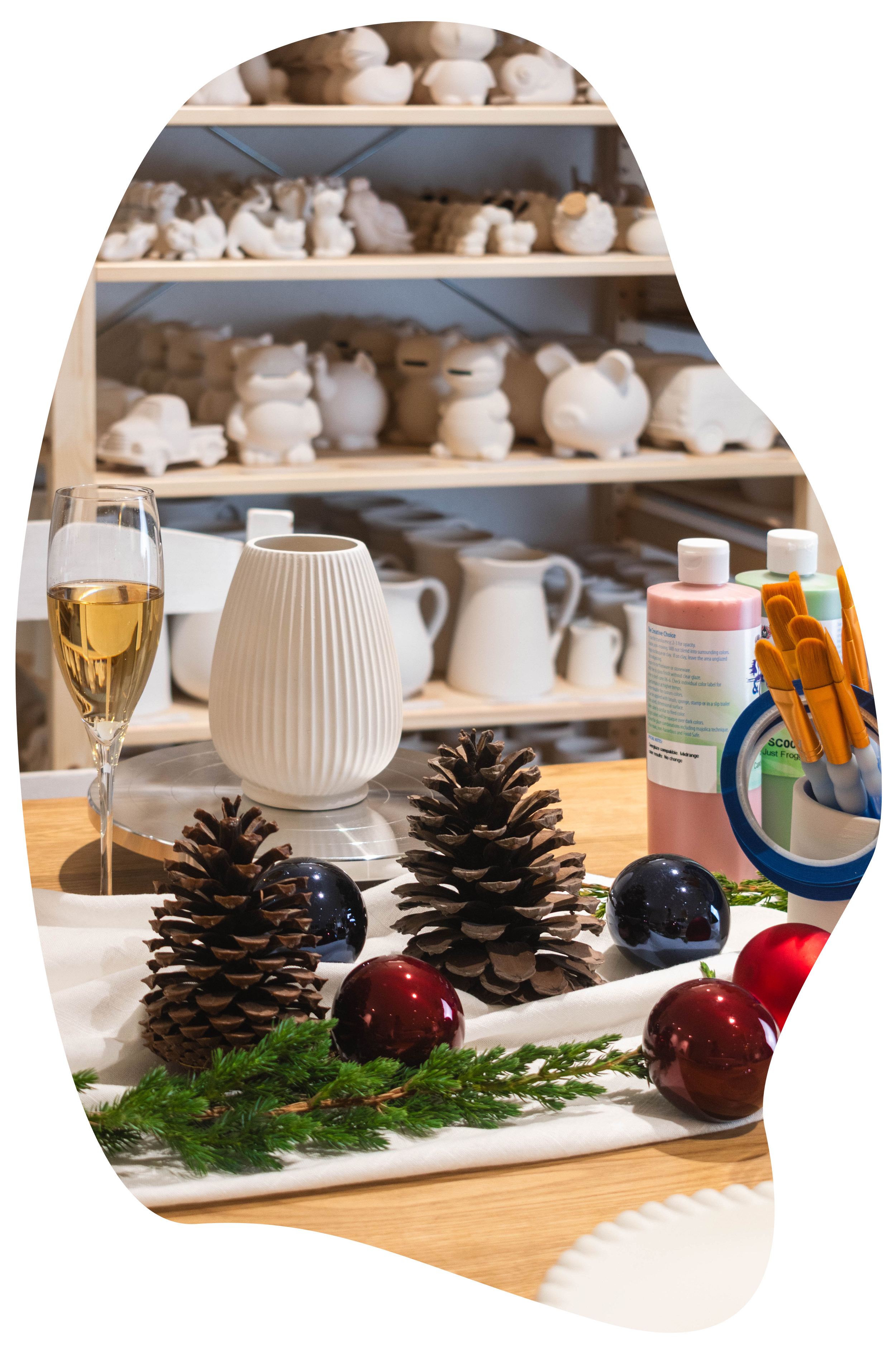 Weihnachtsdekoration mit Tannenzapfen, roten und blauen Weihnachtskugeln, Gläsern, Kerzen und künstlichen Pflanzen auf einem Tisch, im Hintergrund sind handgefertigte Porzellanfiguren auf Regalen.