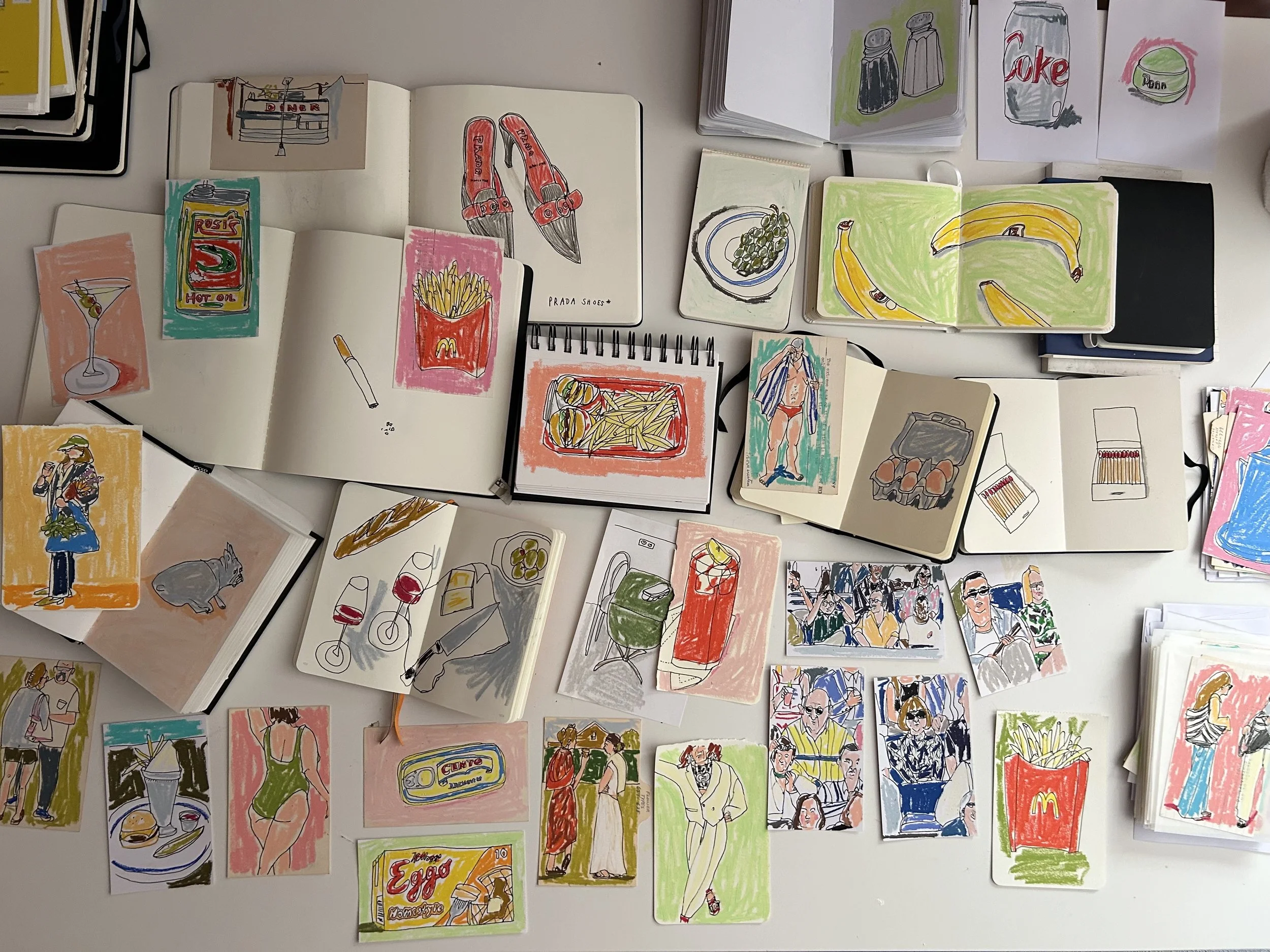 Collection of colorful hand-drawn sketches of food, drinks, people, and objects spread across a white table, including fast food items like fries, burger, and soda, as well as beverages, snacks, and scenes of people dining and socializing.