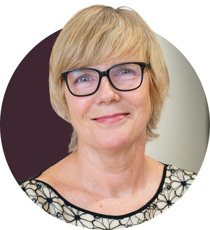 A middle-aged woman with blonde hair wearing glasses and a black and white patterned top, smiling at the camera.