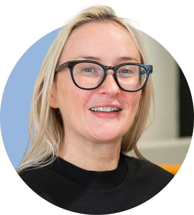 A woman with blonde hair, wearing glasses and a black shirt, smiling at the camera.