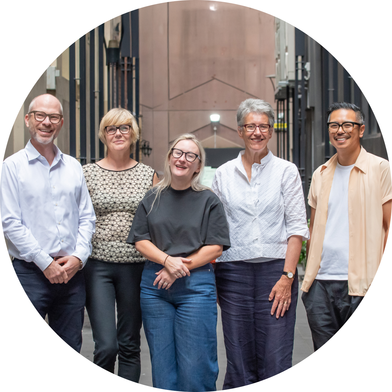 Five people standing together in a laneway, smiling, and facing the camera.