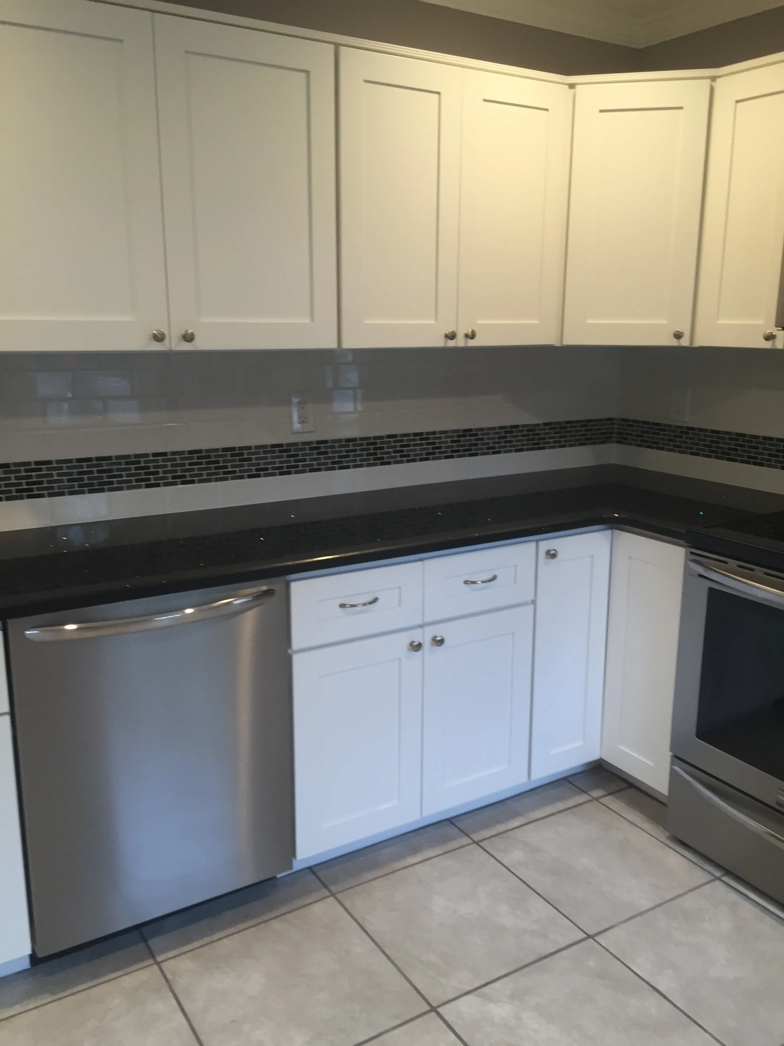 Kitchen with white cabinets, black granite countertops, stainless steel dishwasher, and electric stove, tiled floor, and a decorative tile backsplash.