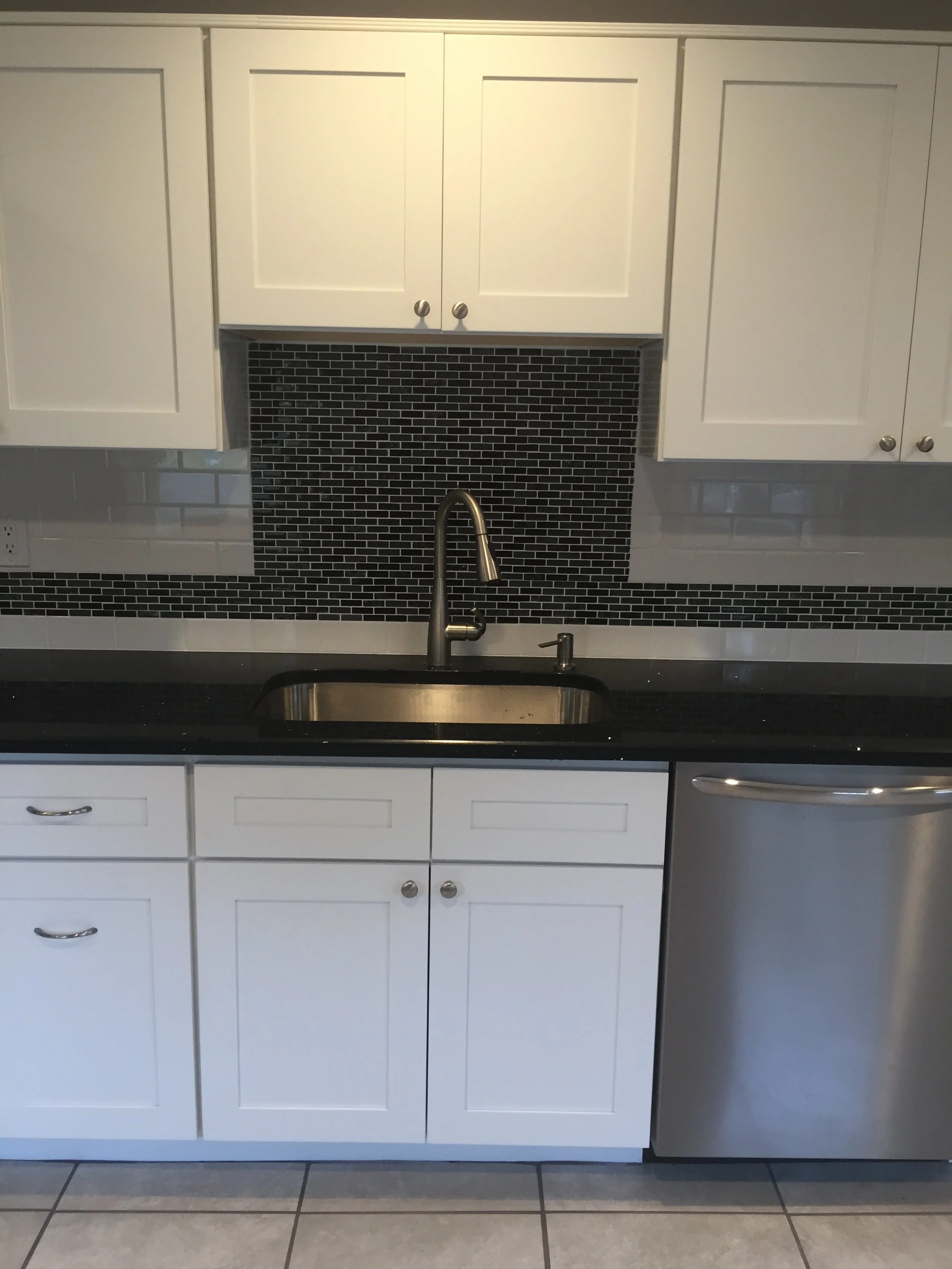 Kitchen with white cabinets, a black countertop, a stainless steel sink, a black tile backsplash, a stainless steel dishwasher, and tiled floor.