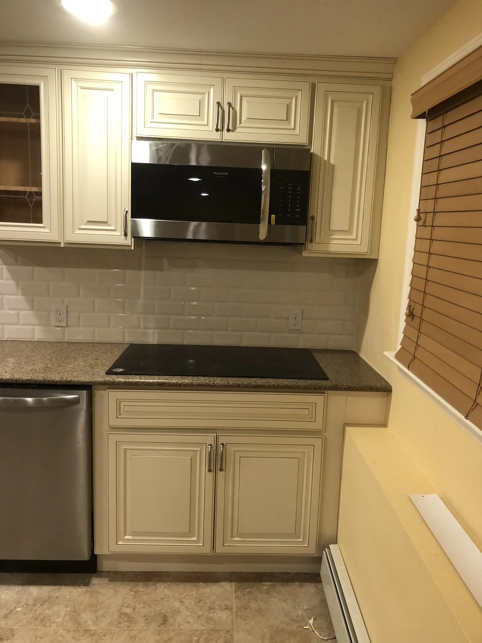 Kitchen with cream-colored cabinets, a microwave, a granite countertop, a stove top, a dishwasher, and a window with wooden blinds.
