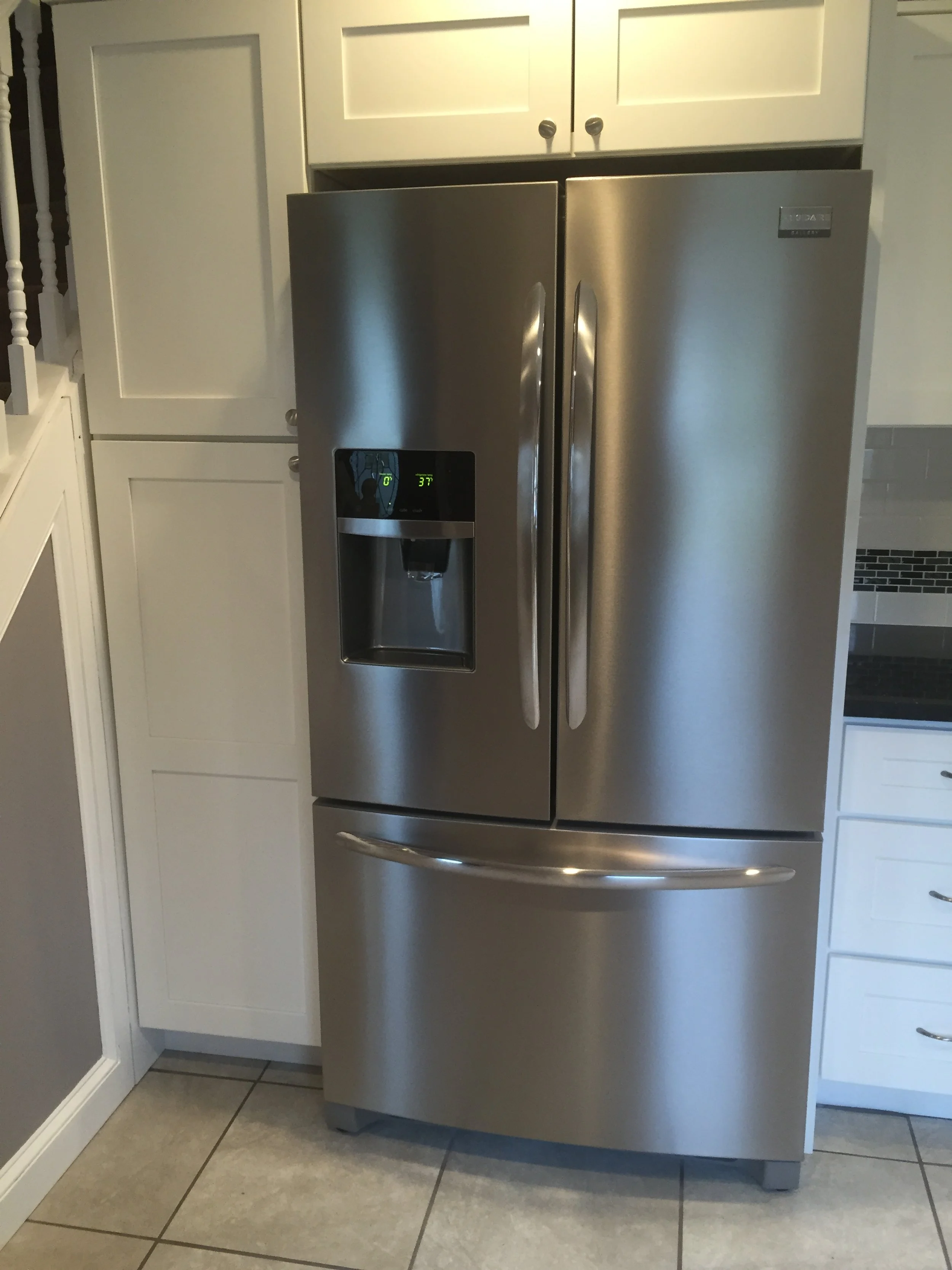 Stainless steel side-by-side refrigerator in a kitchen with white cabinets and tiled floor.