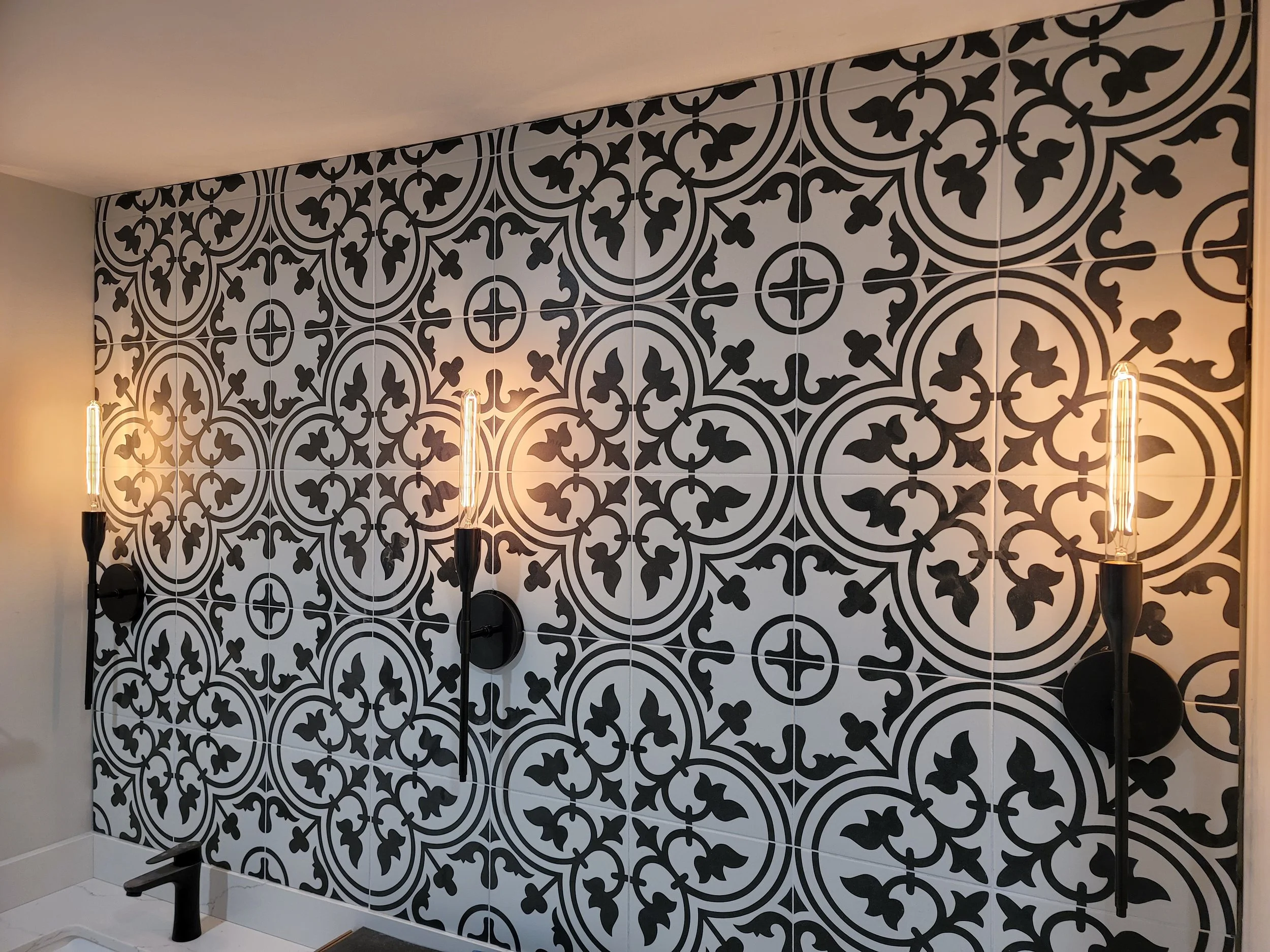 Decorative black and white patterned tile wall with three wall-mounted sconces and exposed filament light bulbs