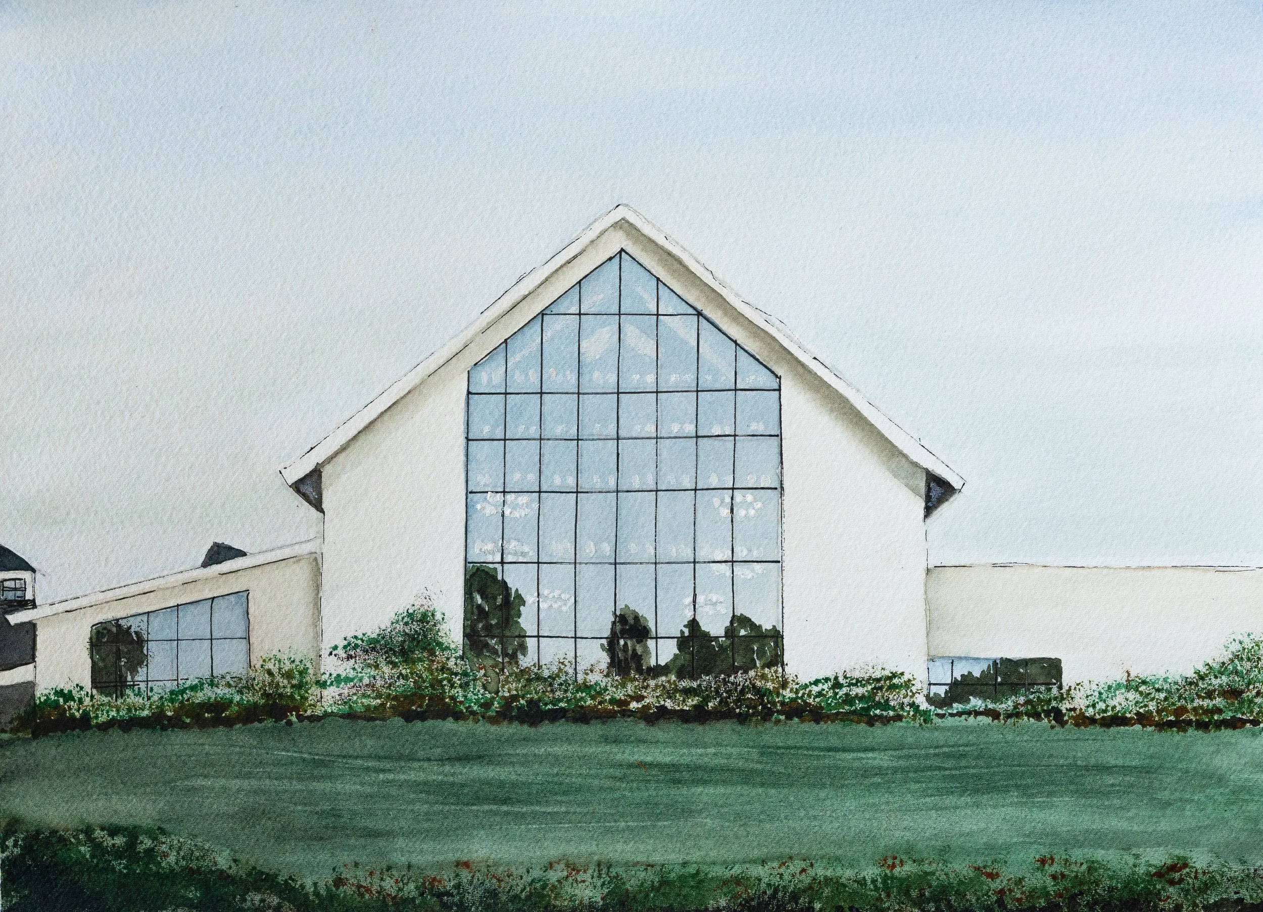 A modern building with large glass windows and a triangular roof, surrounded by trees and greenery.