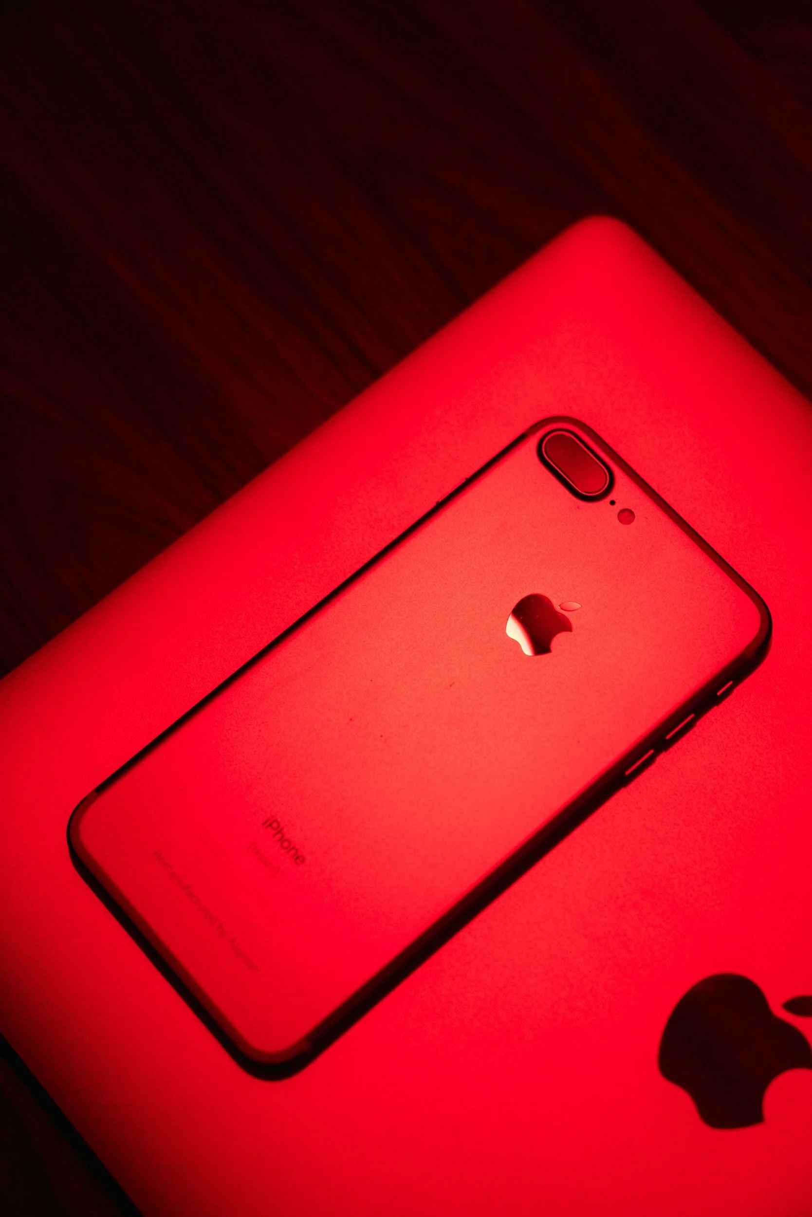 Close-up of a red iPhone with a dual camera and flash, displaying the Apple logo on the back, placed under red lighting.