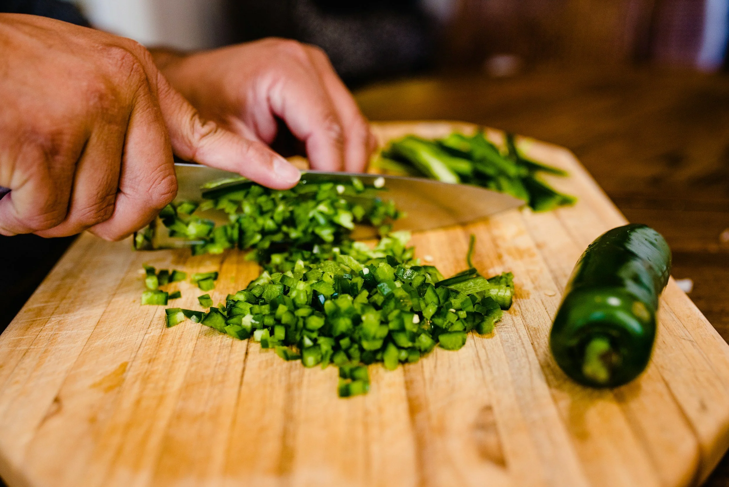 Fresh jalapenos being chopped on a cutting board for chili prep