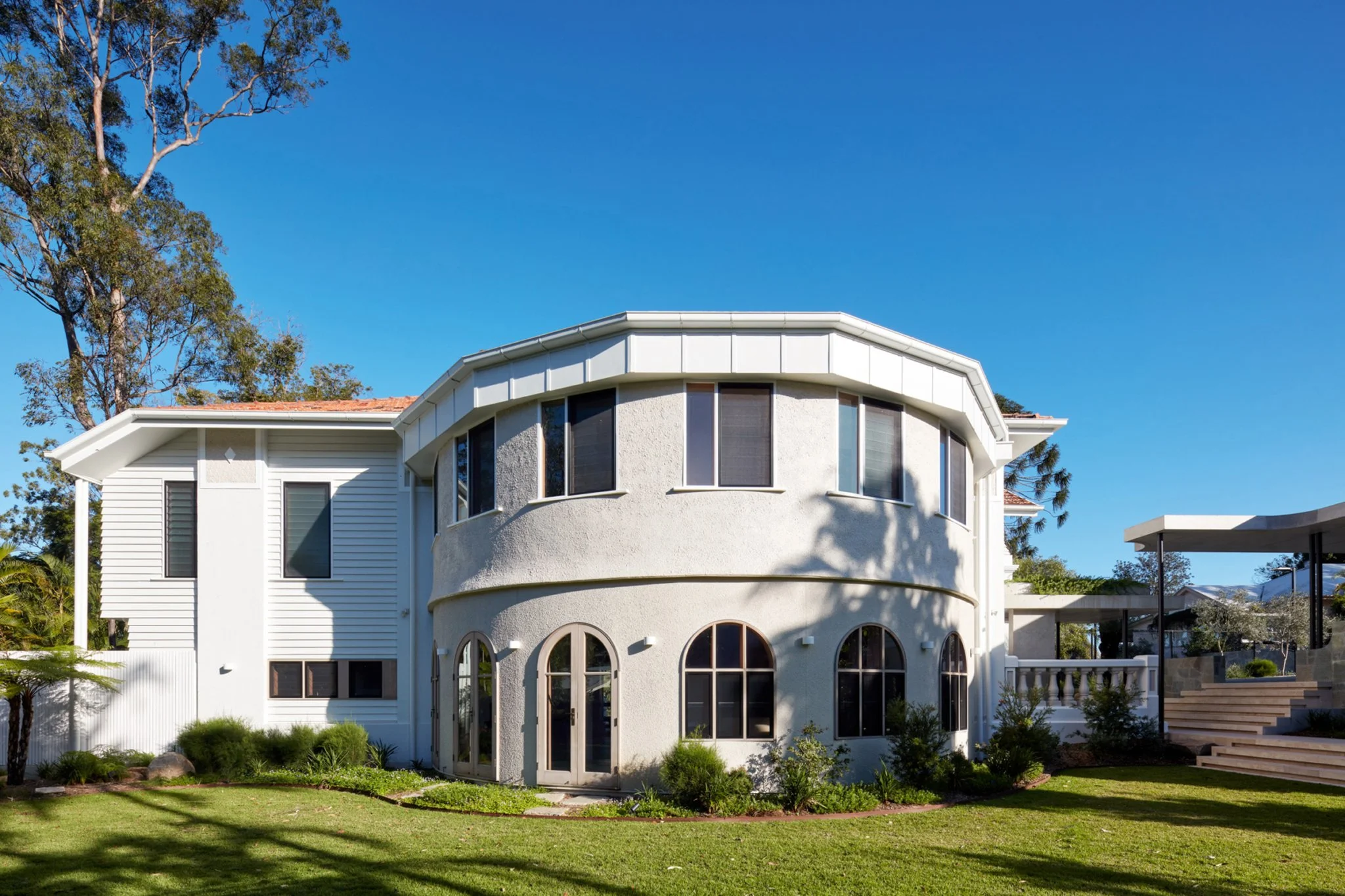 A large, modern house with curved walls, multiple windows, and a well-maintained front yard.