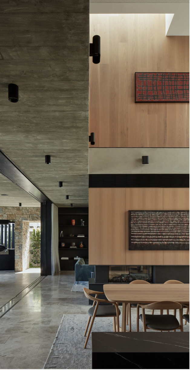 Modern living room with wood-paneled walls, contemporary artwork, a fireplace, and dining area with a wooden table and chairs.