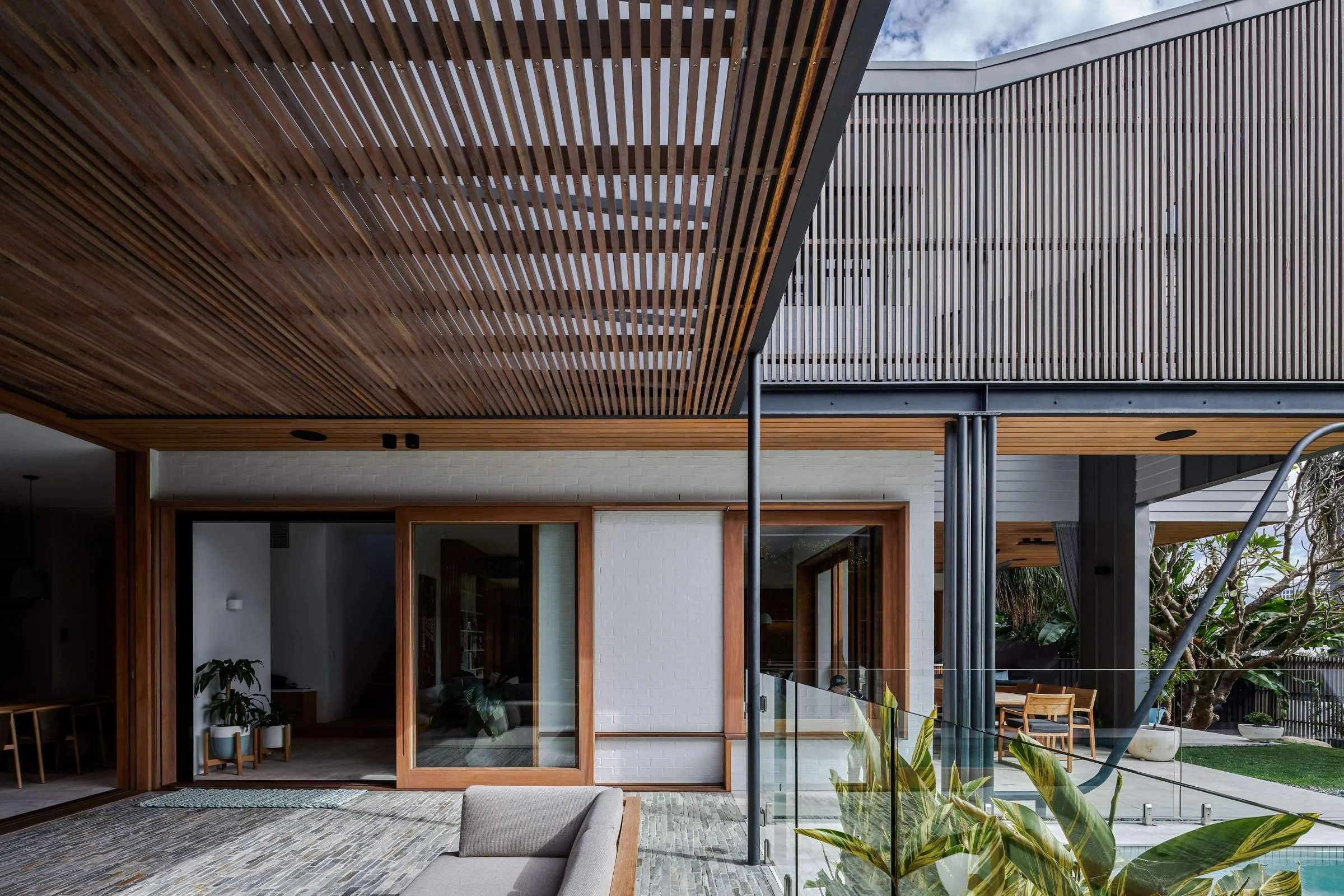 Contemporary house with large sliding glass doors, wooden paneling, and an outdoor sitting area with chairs and plants.