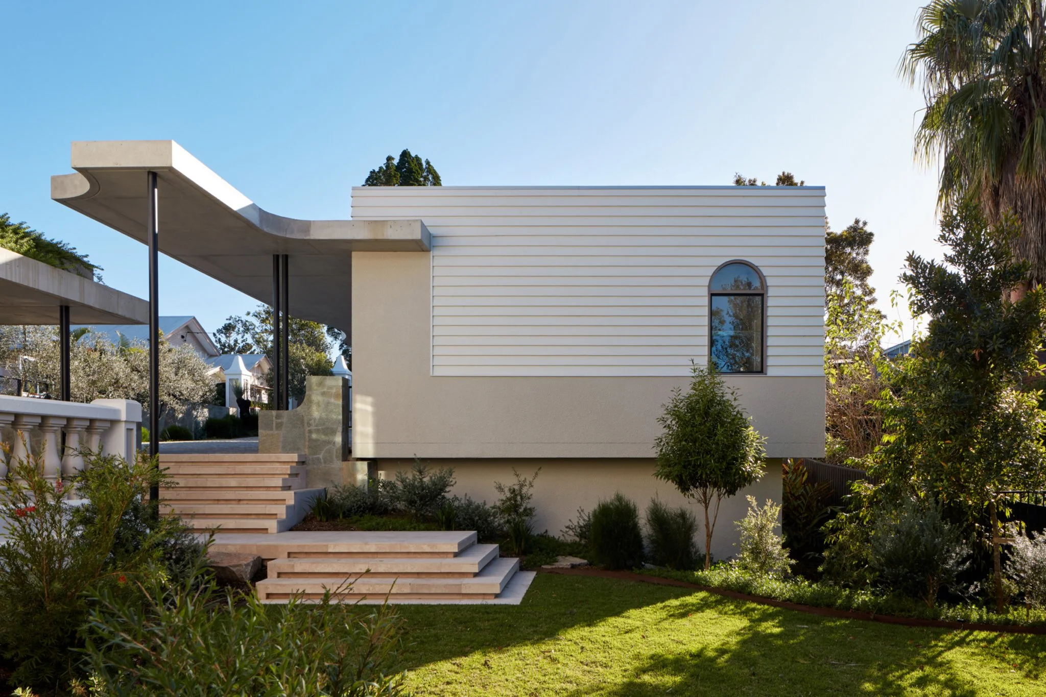 Modern house with white exterior, black window, and landscaped front yard with trees and bushes.