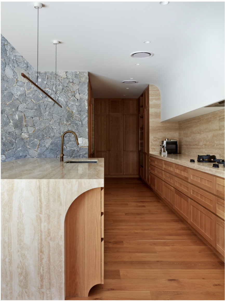 Modern kitchen with wooden cabinets, marble countertops, wood flooring, stone backsplash, and white ceiling with recessed lighting and hanging light fixture.