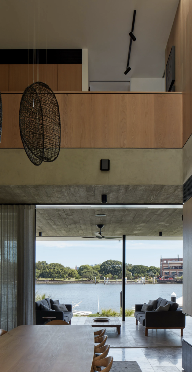 Living room with large glass sliding doors overlooking a waterway, with sofas and a hanging wicker chair.