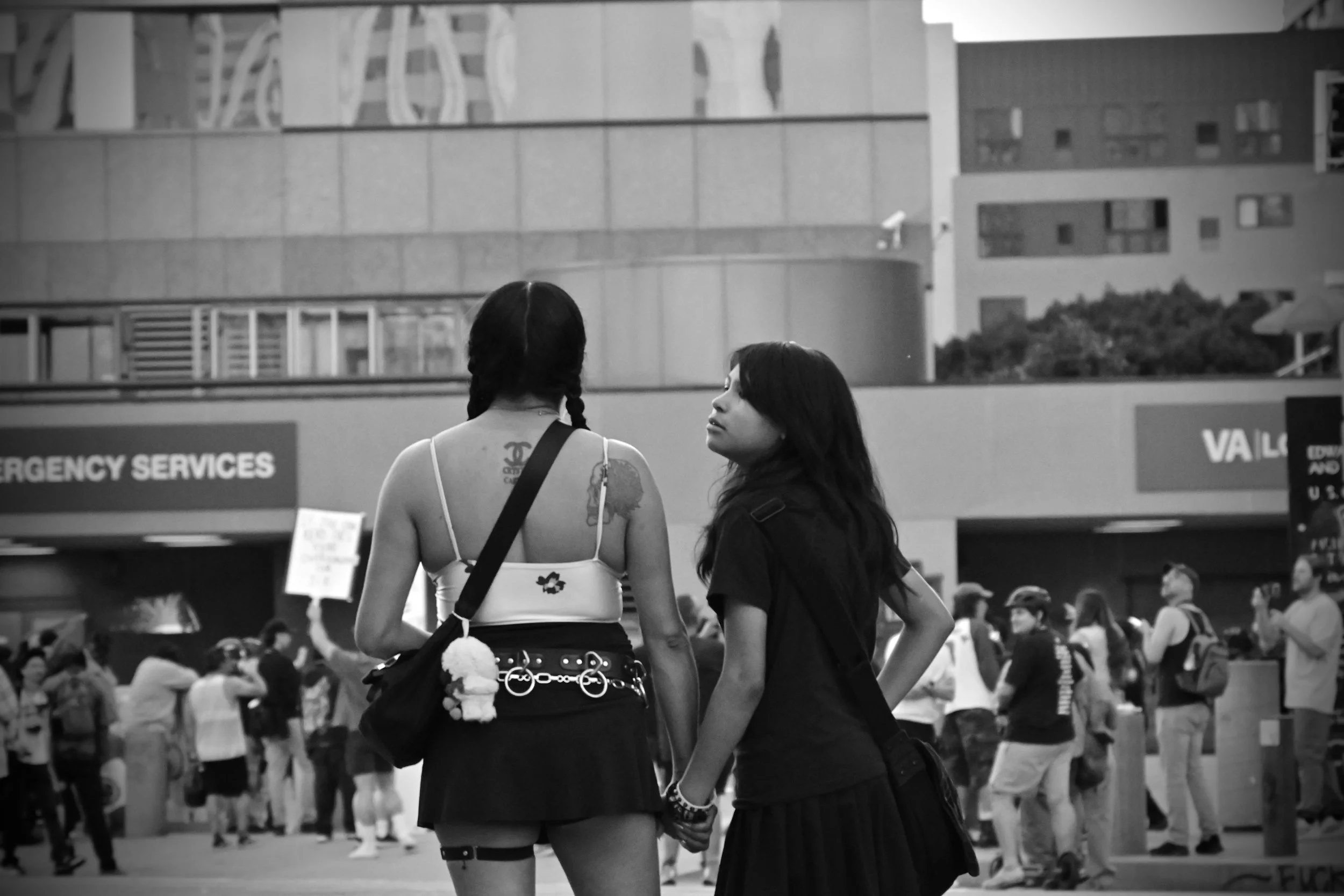 Two young women hold hands as ICE’s Special Response Team deploys from the BATT-X, a quiet gesture reflecting both fear and solidarity among protesters. (Los Angeles, 2026)