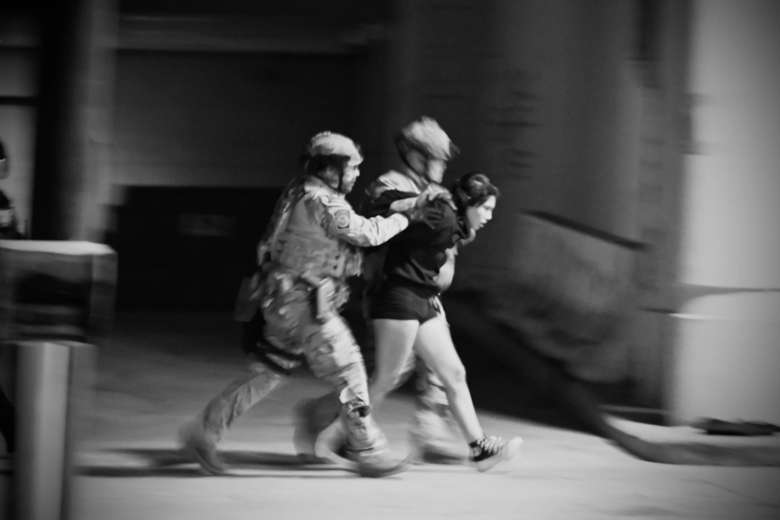 The protester arrested by ICE is escorted in handcuffs into the detention center. Behind her, a DHS agent carries her flag and backpack. (Los Angeles, 2026)