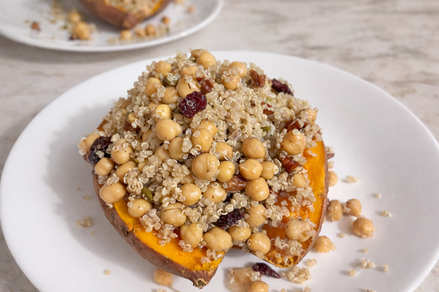 Roasted sweet potato stuffed with quinoa, chickpeas, dried cranberries, and chopped nuts, served open-faced on a white plate.