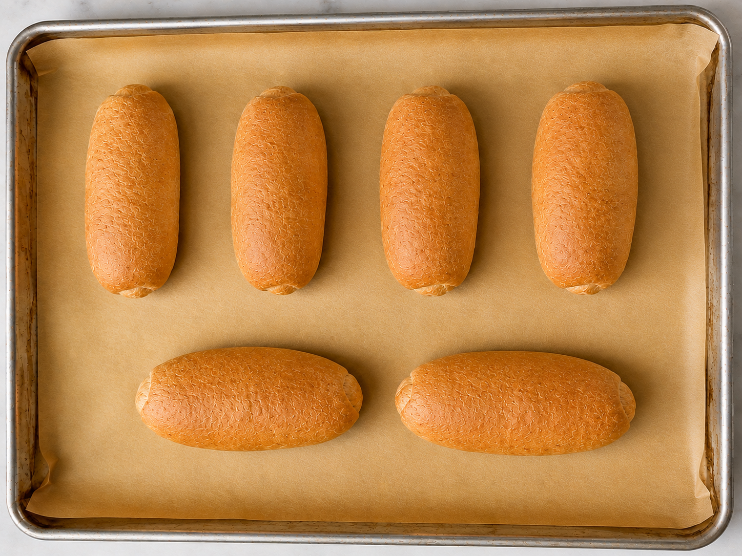 Six baked whole wheat sub rolls on a parchment-lined baking sheet after baking.