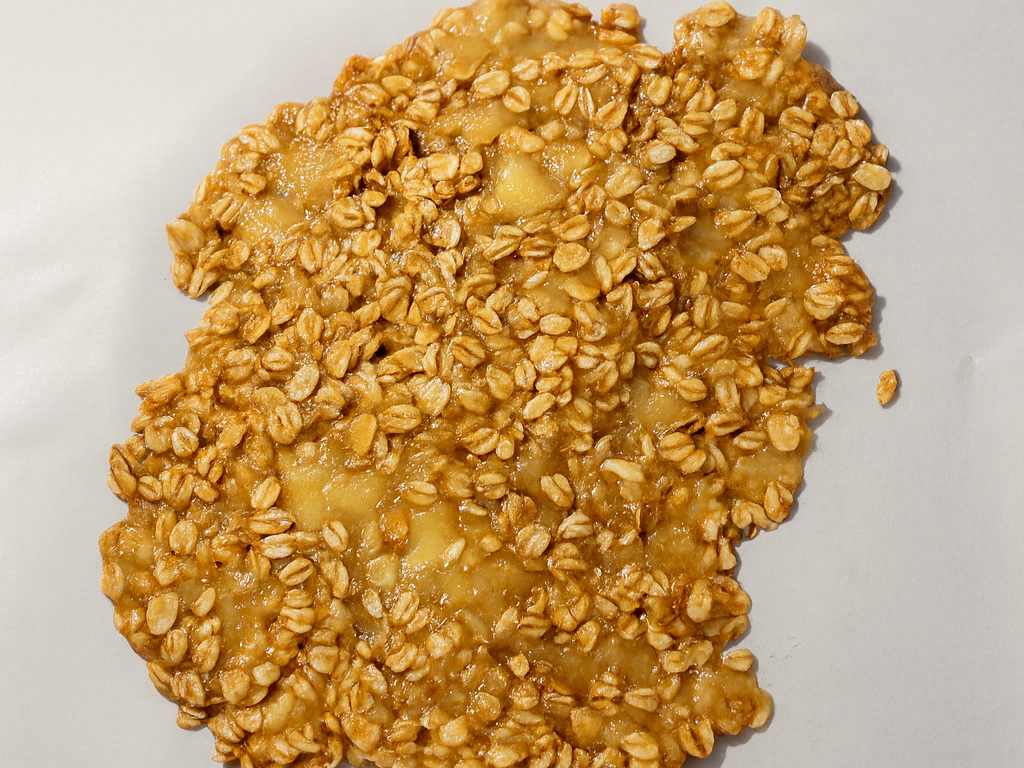 Close-up of mashed banana and rolled oats mixed with cinnamon and spread in an even layer on a parchment-lined baking sheet before baking.