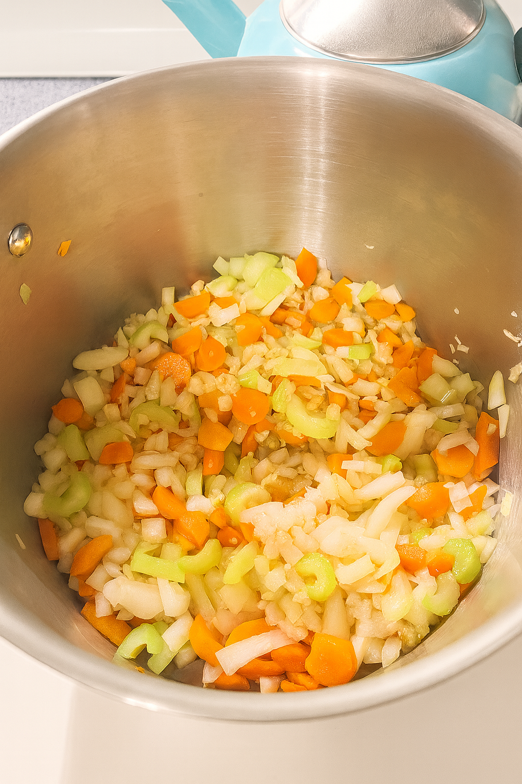 Chopped onions, carrots, celery, and garlic cooking together in a stainless steel pot as the base for golden soup.