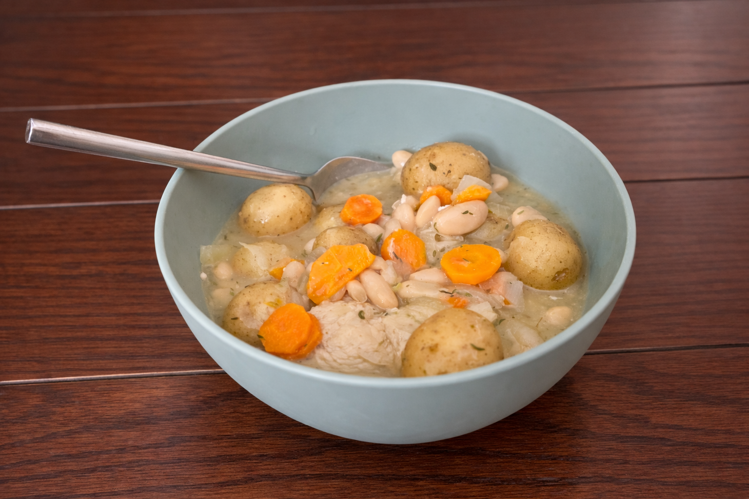Bowl of homemade Dutch oven chicken stew with baby potatoes, carrots, white beans, and chicken in a light broth.