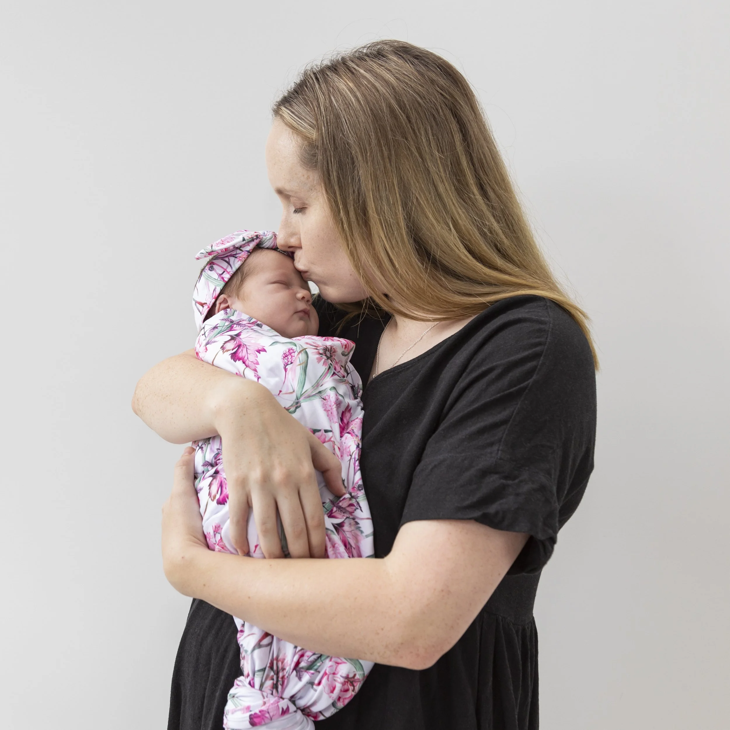 Photo of Mum kissing her newborn baby daughter at home.