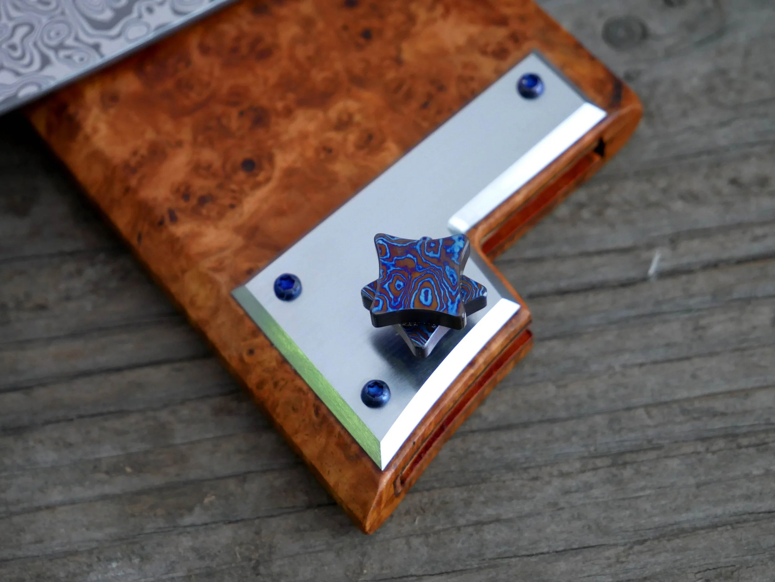 Stainless plate on the amboyna burl saya, held in place with titanium hardware and holding a threaded titanium pin with a Timascus head.