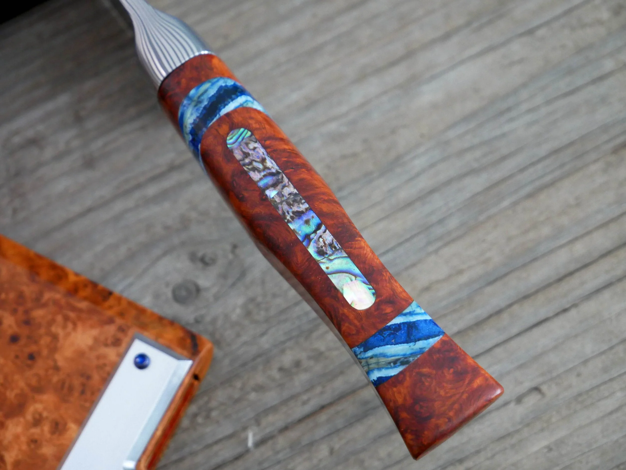 Abalone inlay on the spine of the blood-orange amboyna burl handle, also featuring mammoth tooth spacers.  Handle is hand-finished to a fine grit and shaped in the western style.