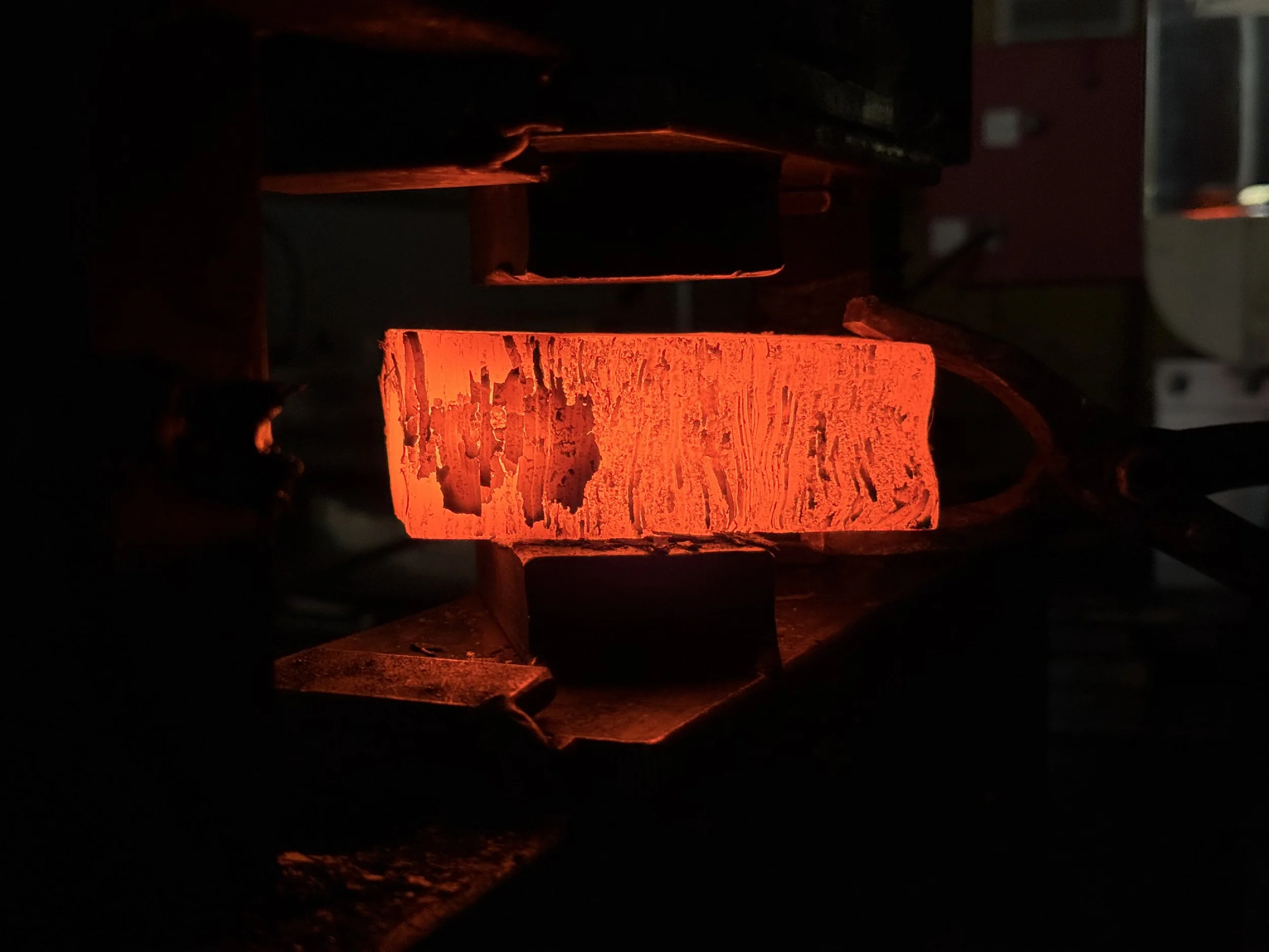 A red hot custom damascus kitchen knife in the manufacturing process of being pressed.