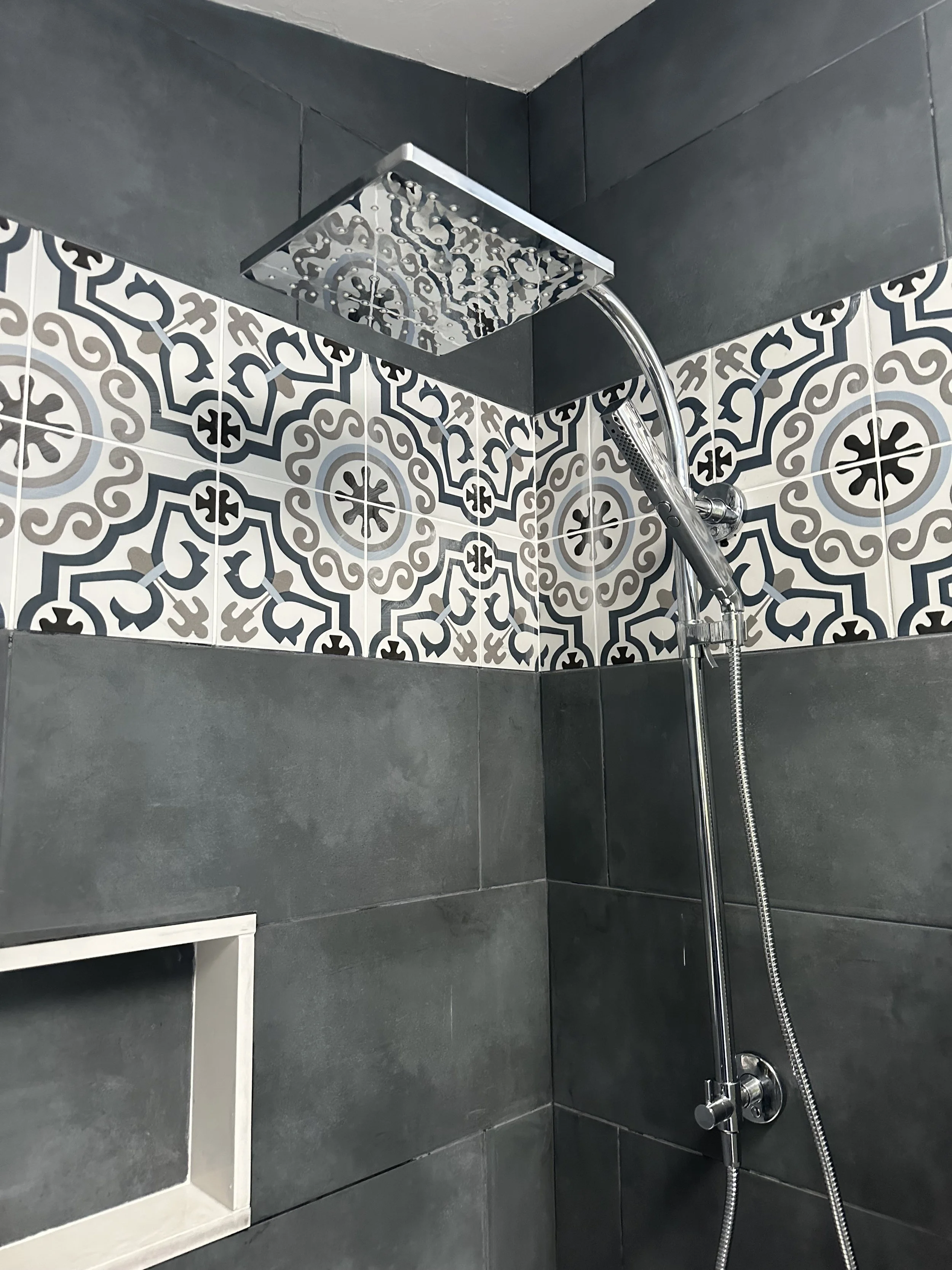 A modern shower with dark gray tiles, a decorative patterned tile strip, a rain showerhead, and a handheld showerhead.