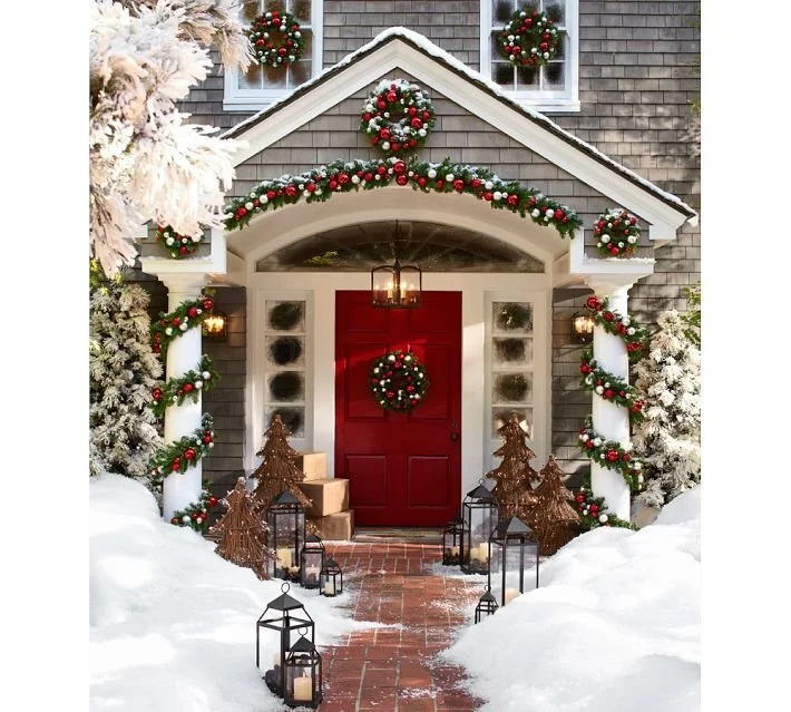 Festively decorated house entrance with a red door, wreath, and Christmas ornaments.