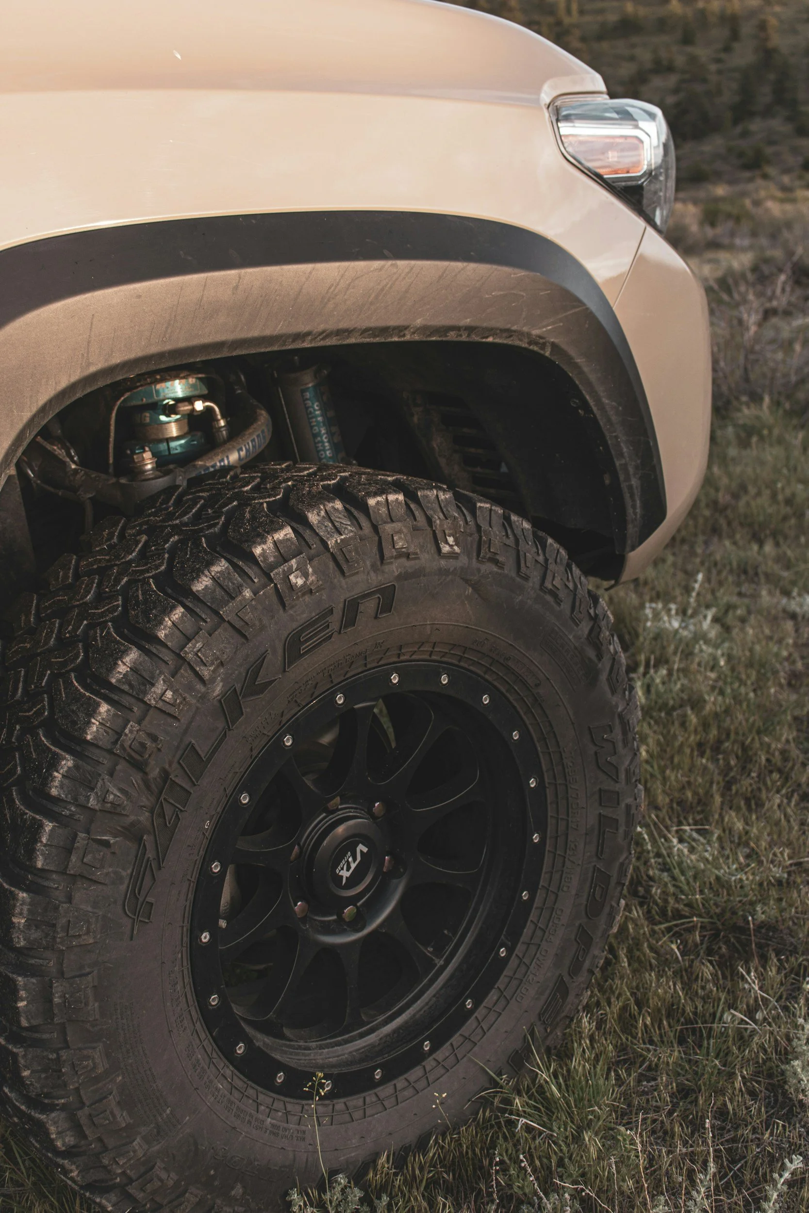 Close-up of a beige off-road vehicle's front wheel with a large, rugged tire on a grassy area.