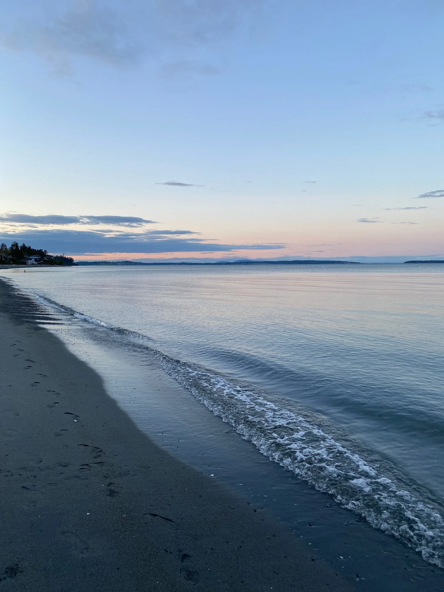 Calm ocean shoreline with sandy beach and pastel sunset sky.
