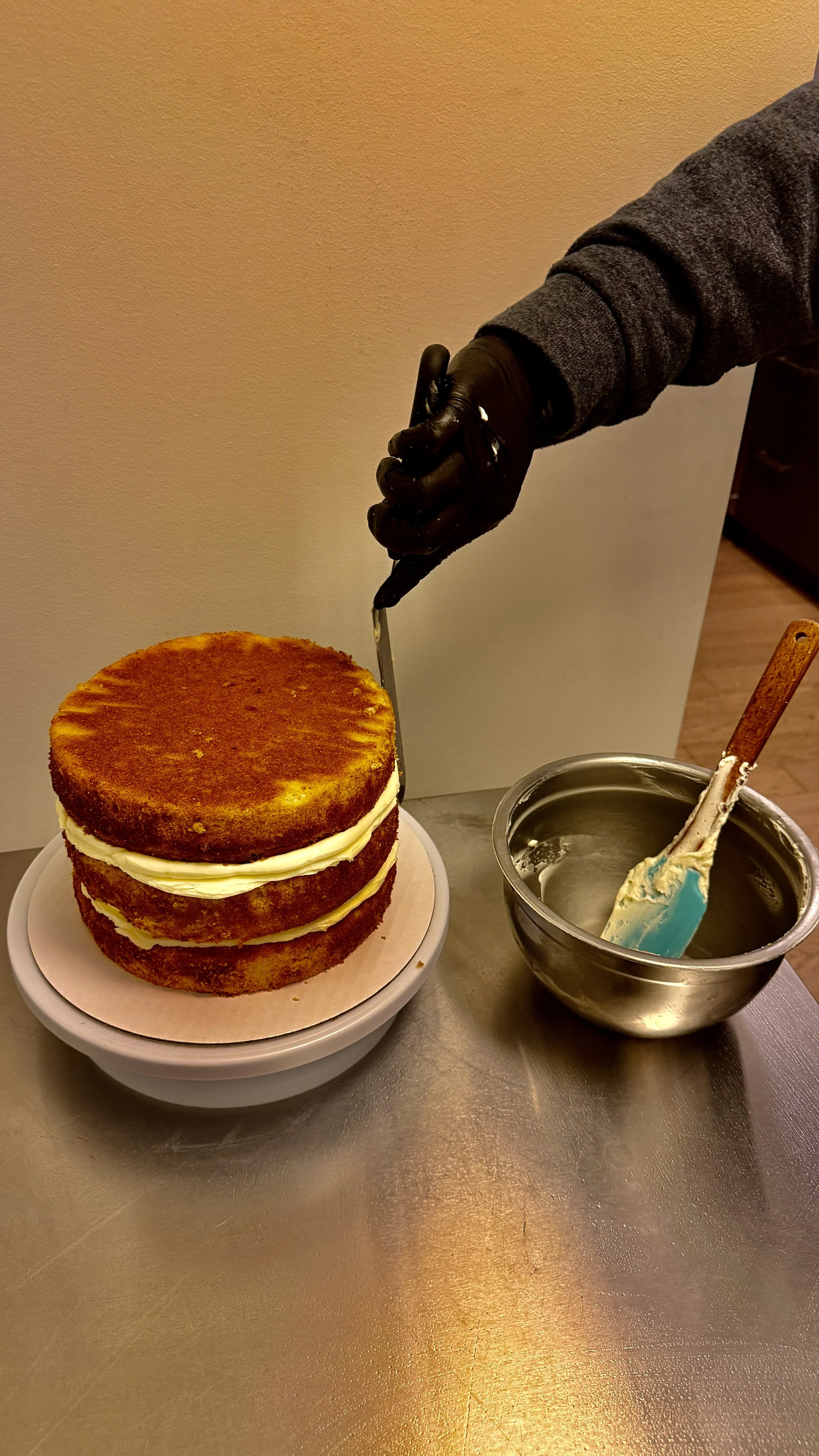 Layered Vanilla Cake with Raspberry filling and Vanilla Buttercream Icing being spread on three tiers in Manhattan, NYC.