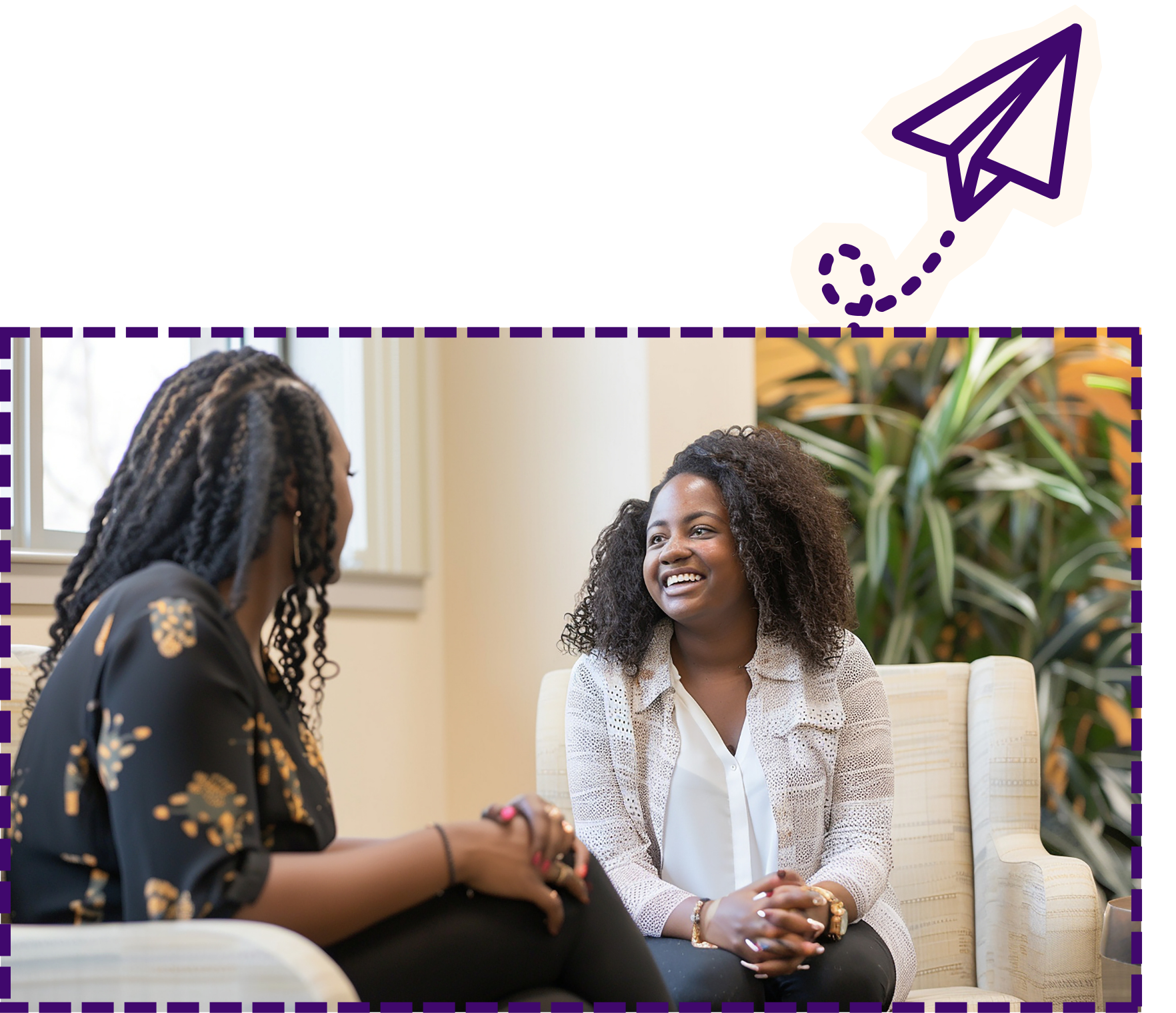 Two women sitting and talking in a bright office or waiting room, with plants in the background. One woman is smiling, wearing a white blouse and a light-colored cardigan; the other has braided hair and is wearing a dark floral top.